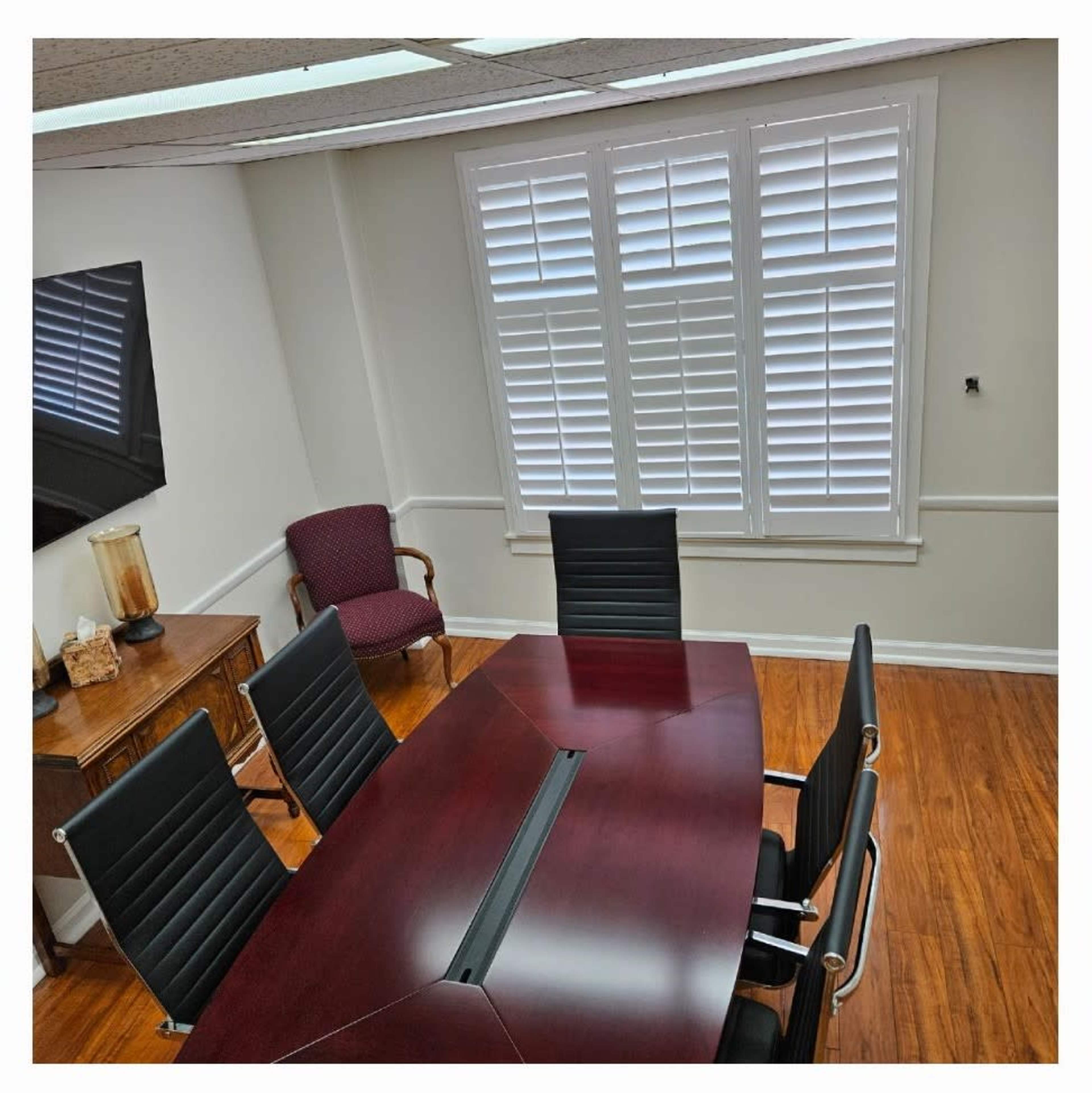 The image shows a conference room featuring a large wooden table surrounded by six black chairs, with a side chair and a cabinet against the wall.