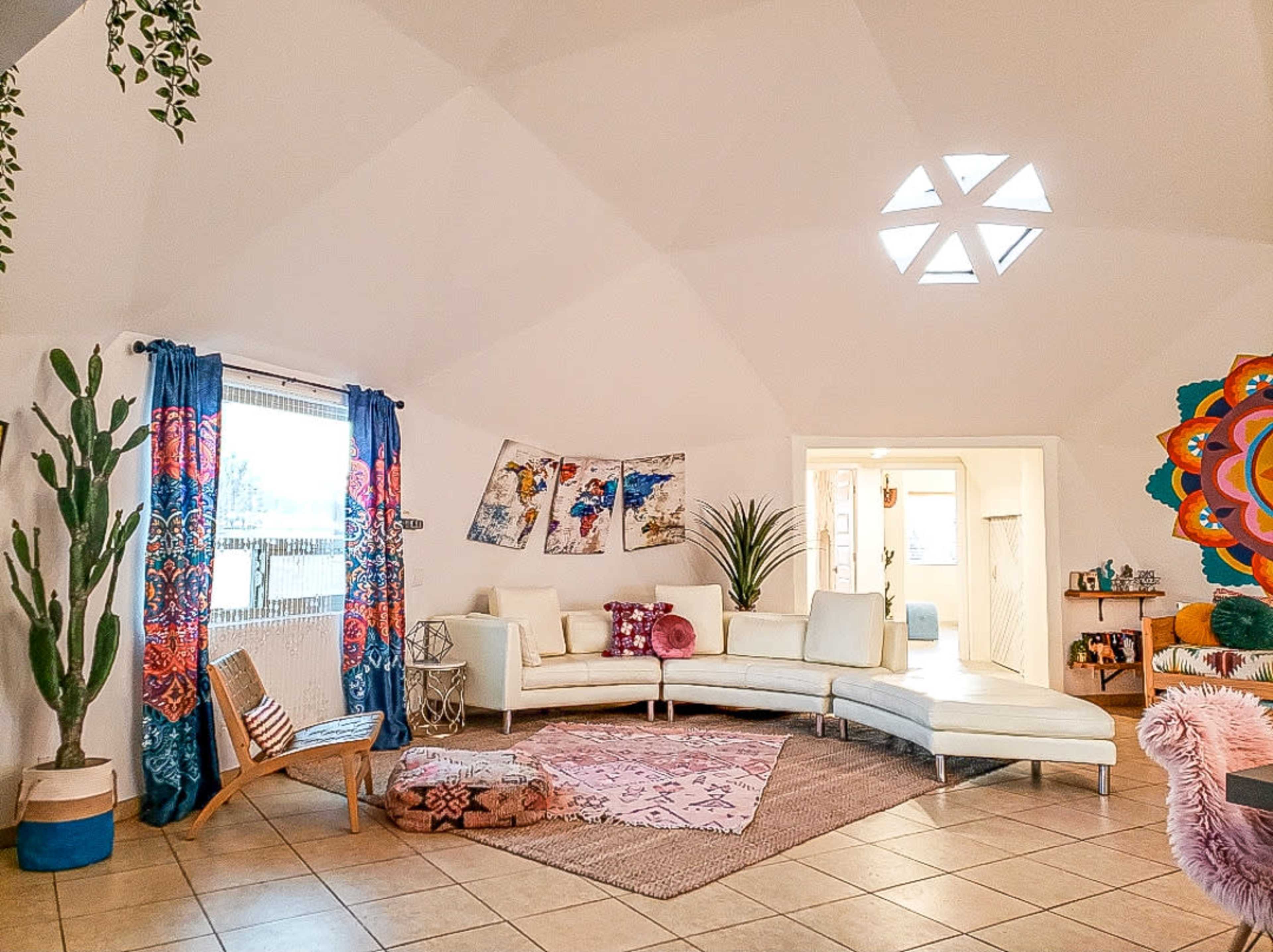 A stylish living room with a curved white sofa, decorative plants, colorful curtains, and artwork on the walls.