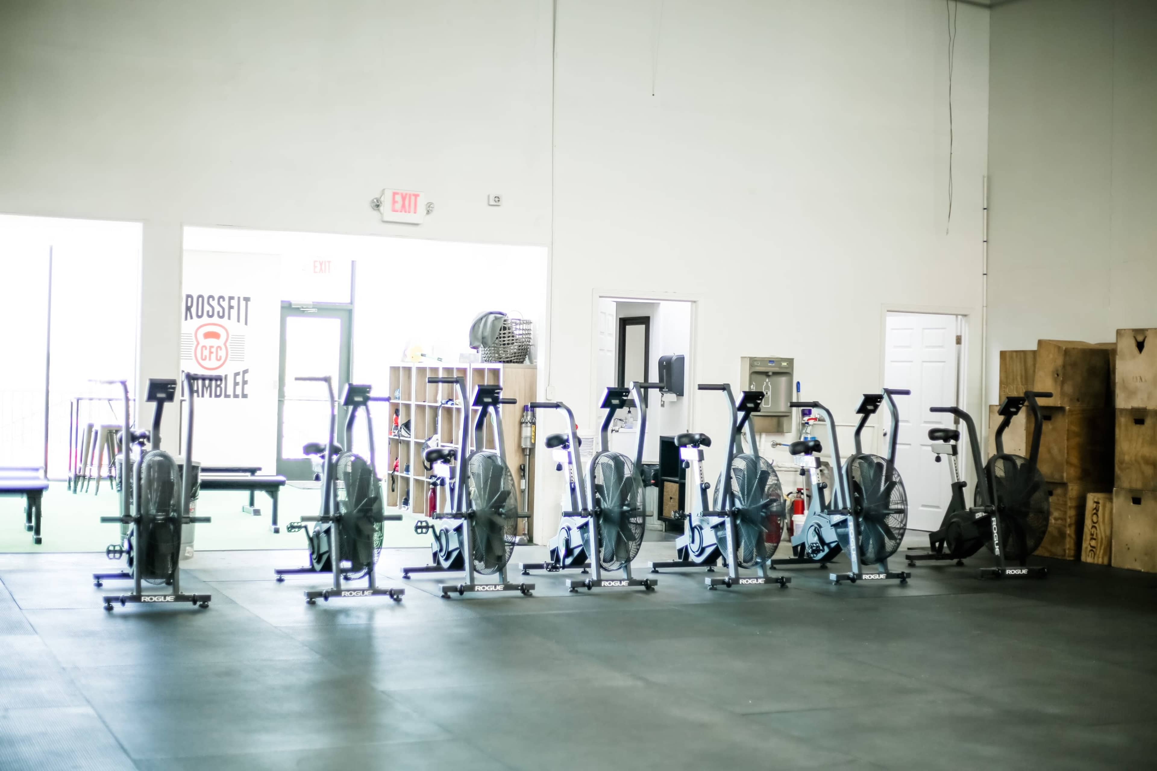 A row of exercise bikes lined up in a gym with open doors and wooden boxes in the background.