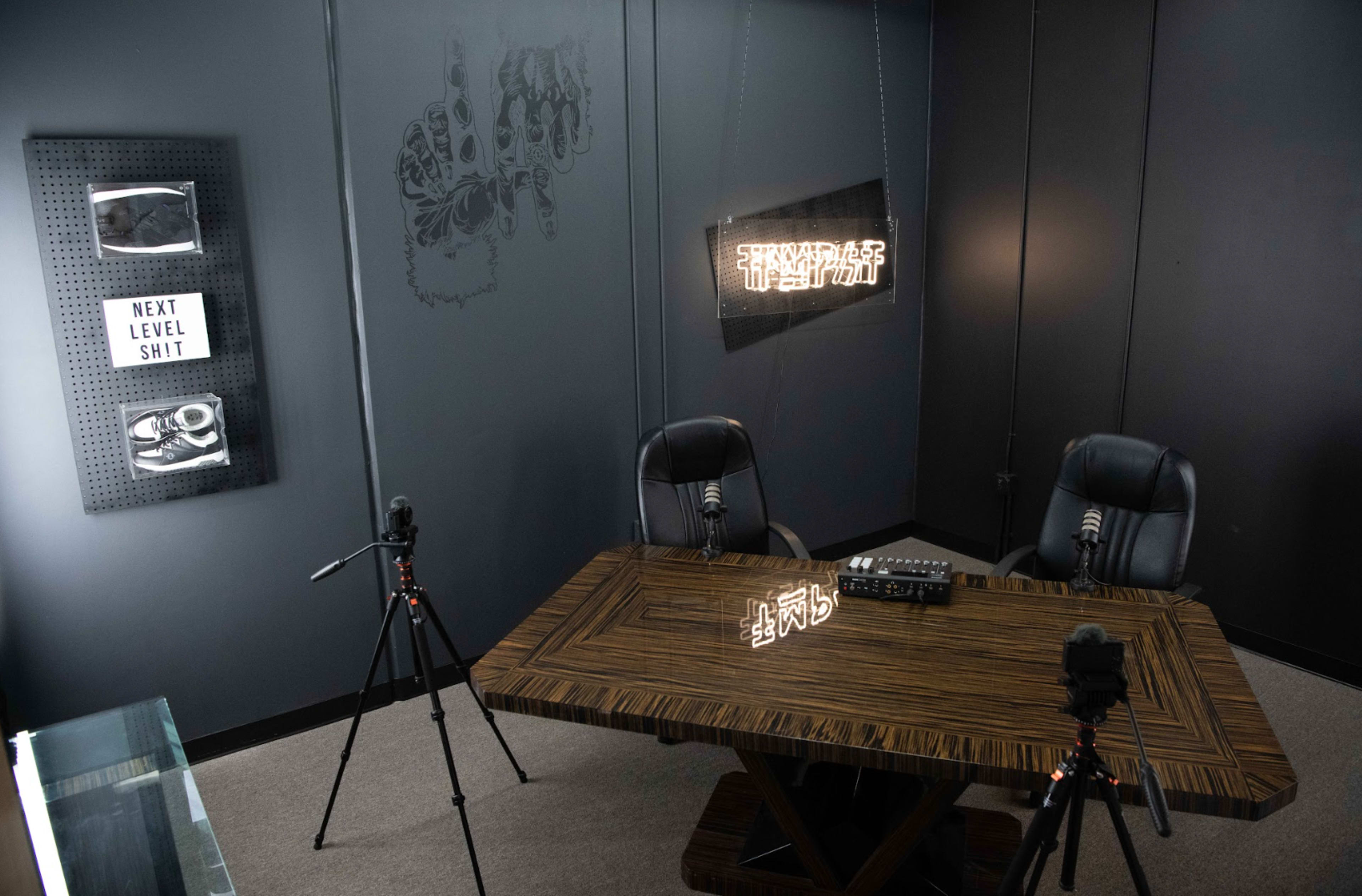 A recording studio setup with a wooden table, two chairs, microphones on stands, and decorative wall art.