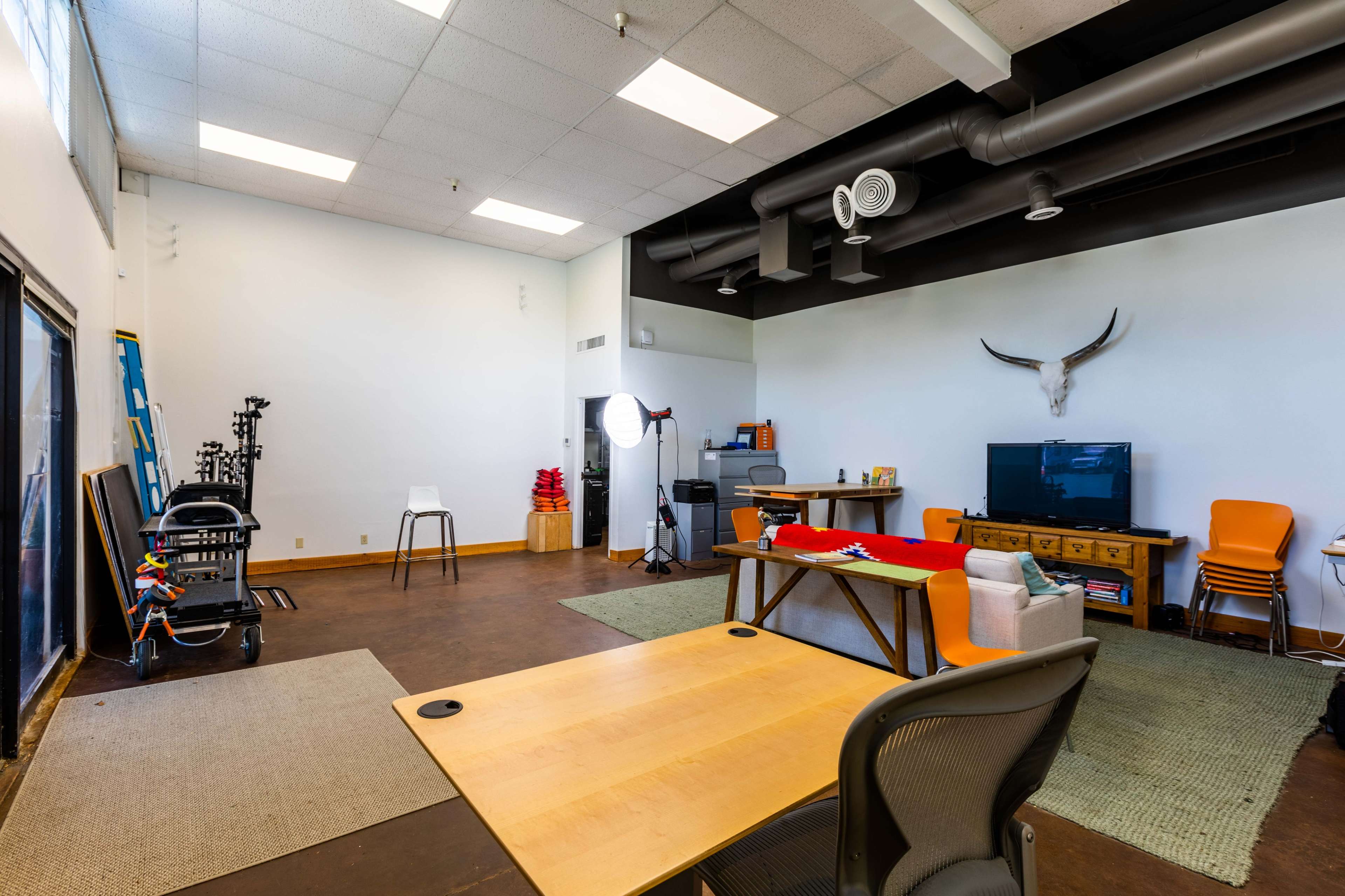 An open office space featuring a wooden table, chairs, a television, and various equipment along with a large wall-mounted decoration resembling animal horns.