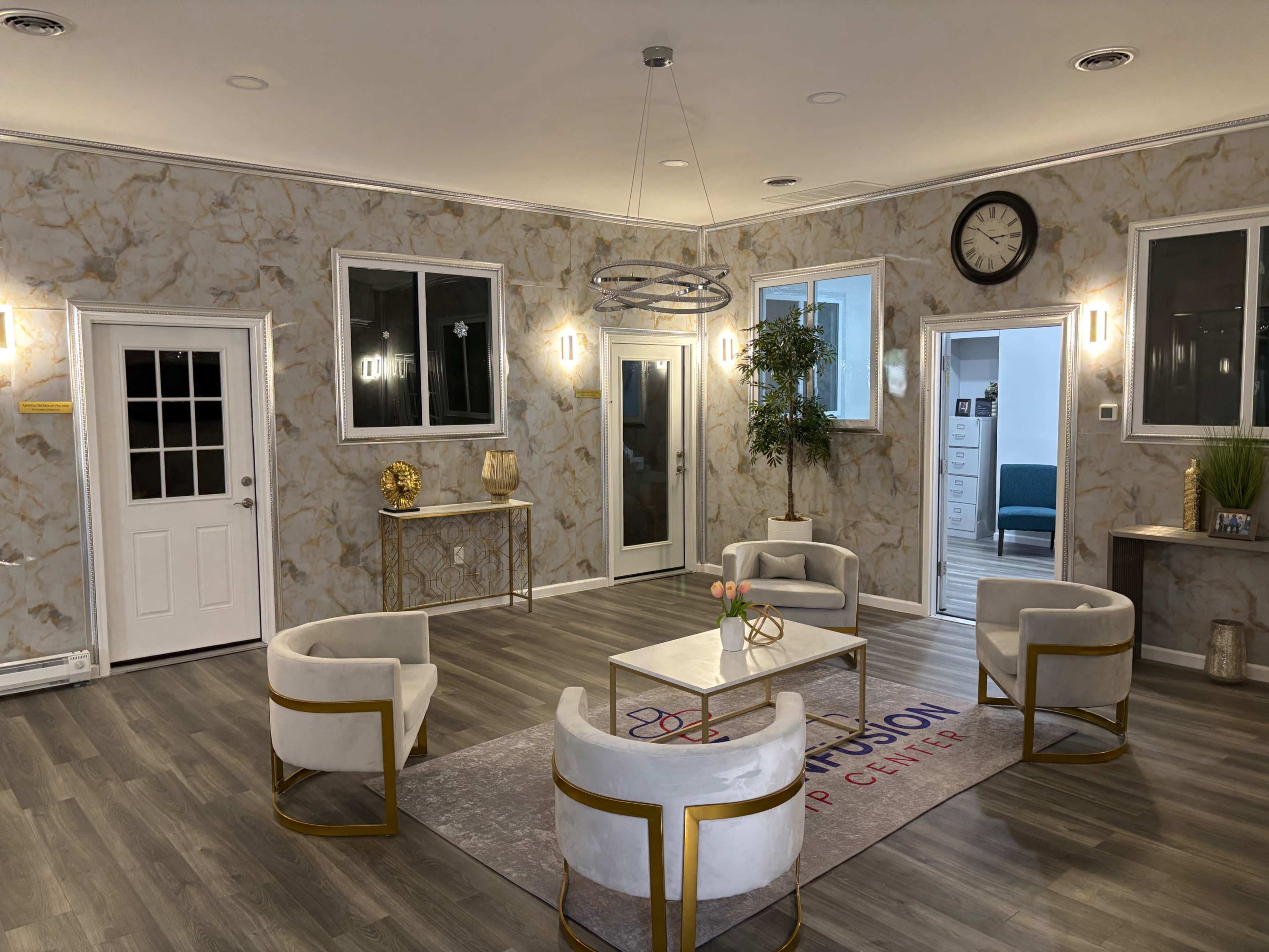 The image shows a modern interior space with marble-patterned walls, a circular light fixture, four white chairs arranged around a coffee table, and several doorways leading to other rooms.