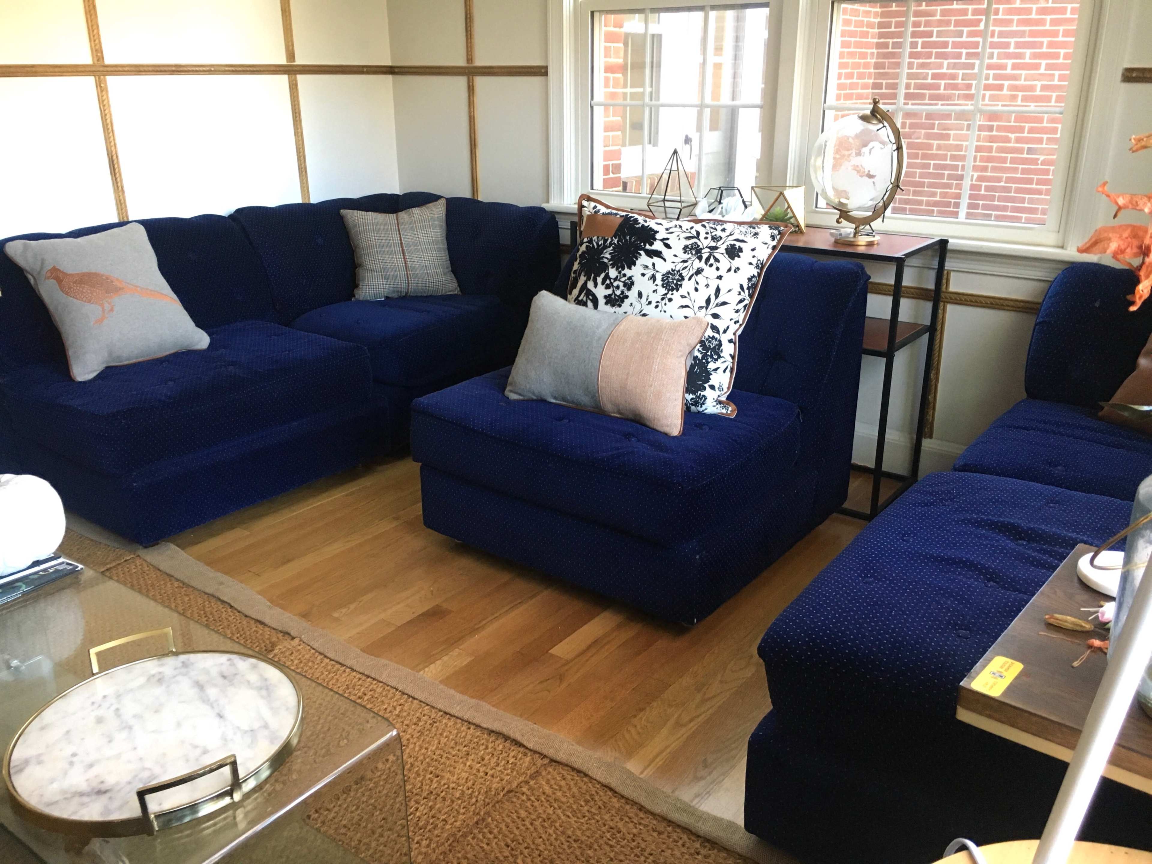 A spacious living room featuring a dark blue sectional sofa arranged around a coffee table on a wooden floor.