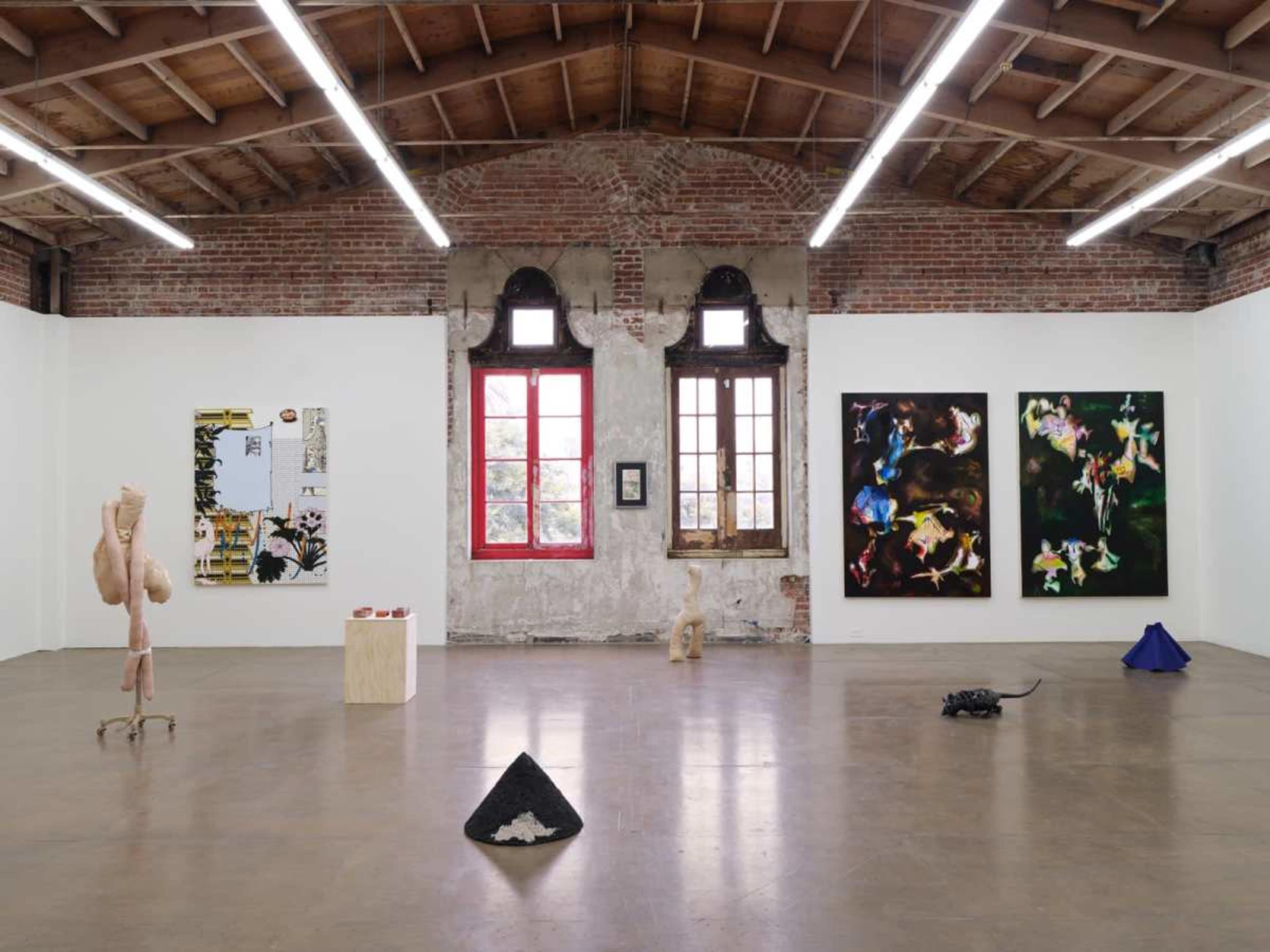 An art gallery featuring various artworks displayed on white walls, with brick accents and large windows.
