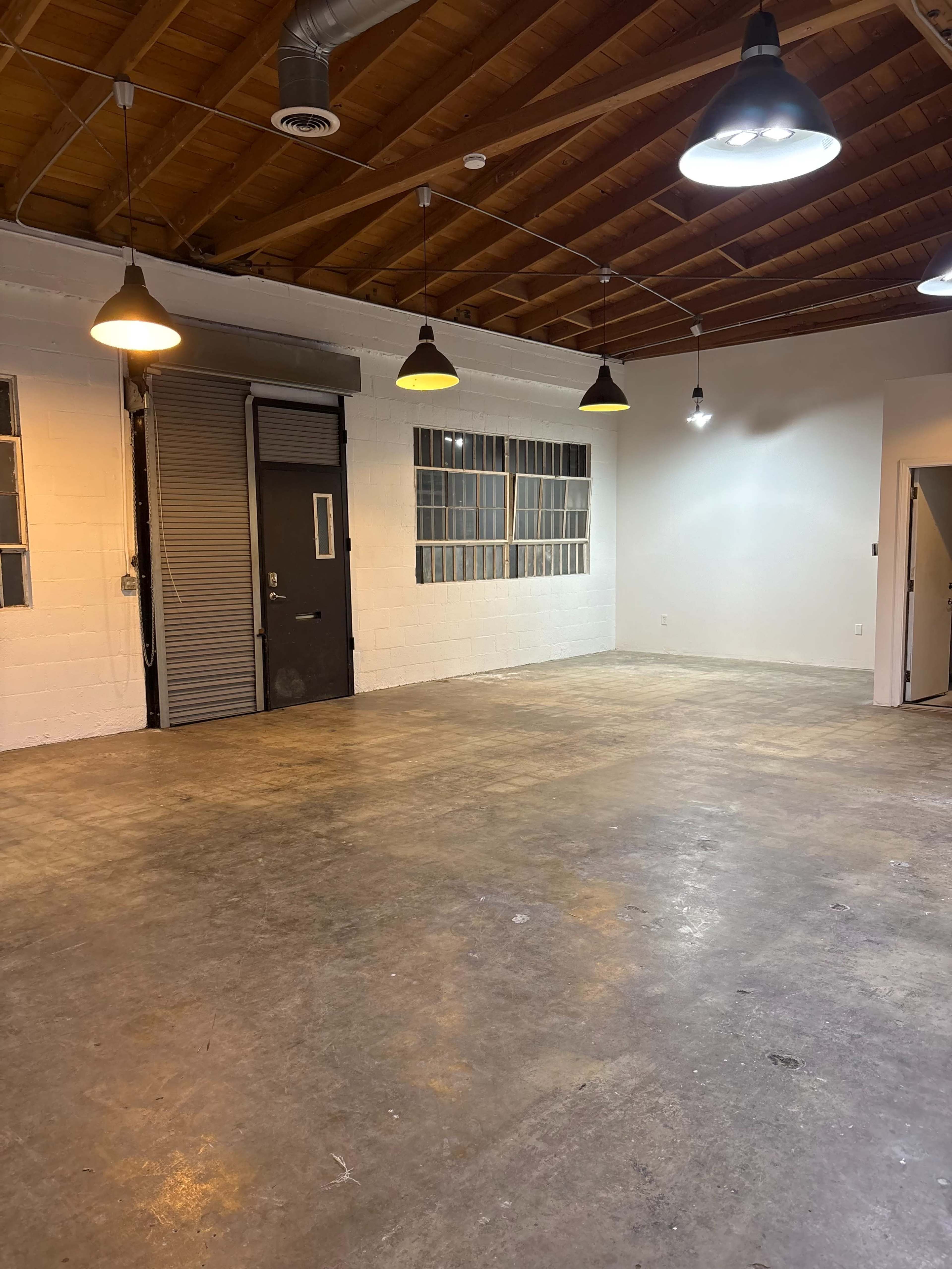 The image shows an empty indoor space with a concrete floor, white walls, and multiple light fixtures hanging from the ceiling.