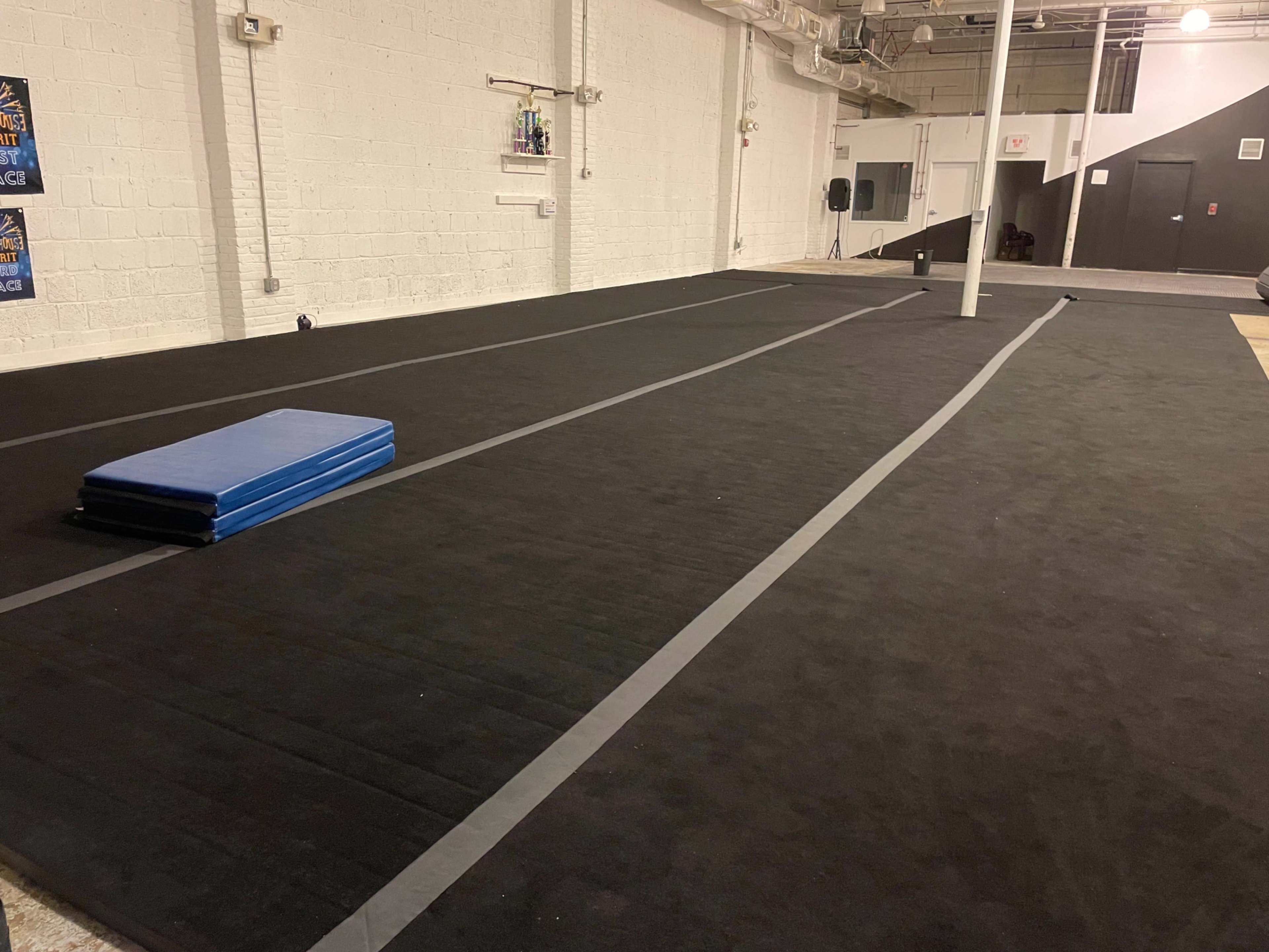 A spacious gymnasium floor with black rubber flooring and a blue gym mat placed on it.