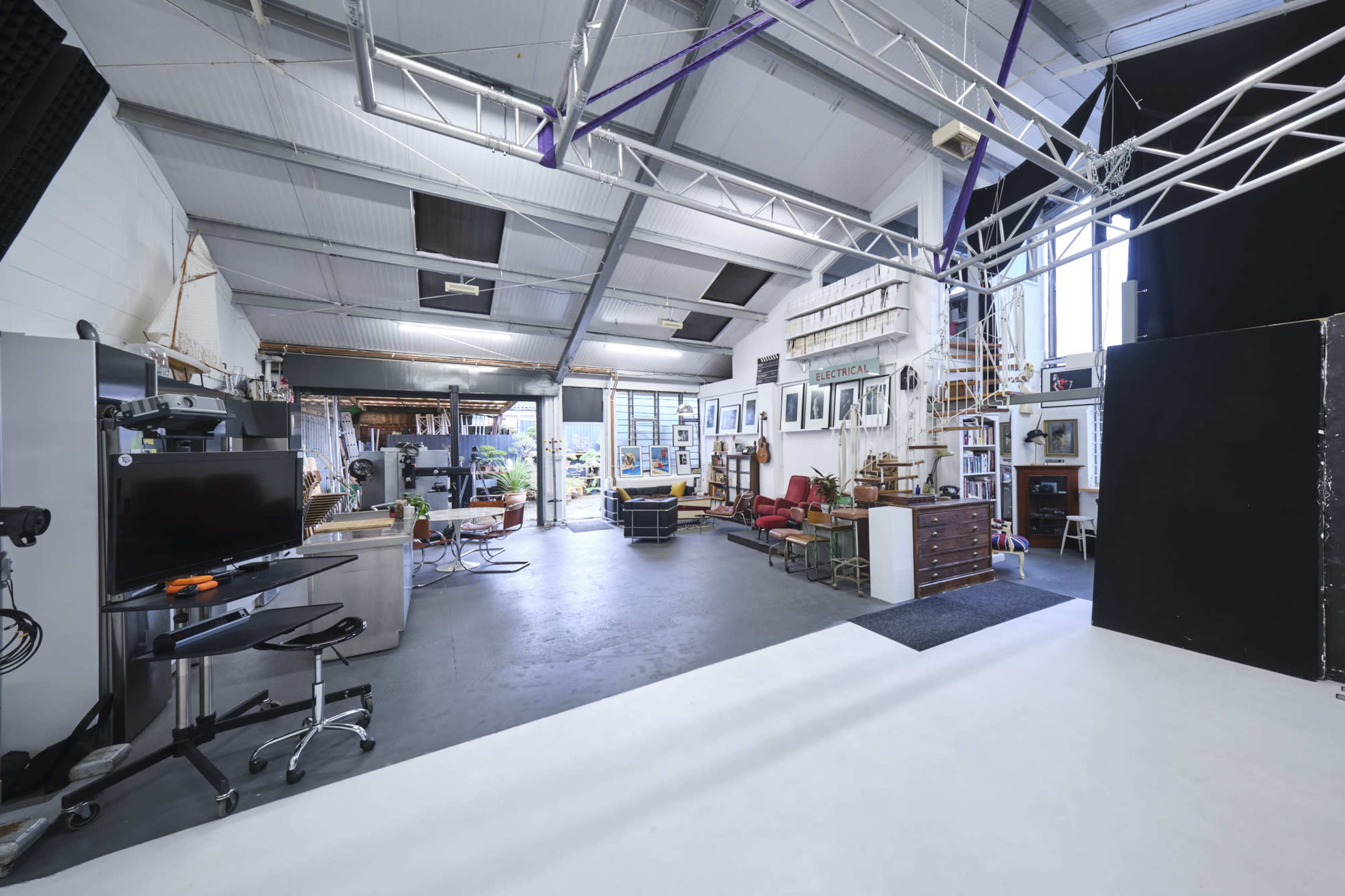 A spacious studio with various workstations, large windows allowing natural light, and eclectic furnishings arranged around the area.