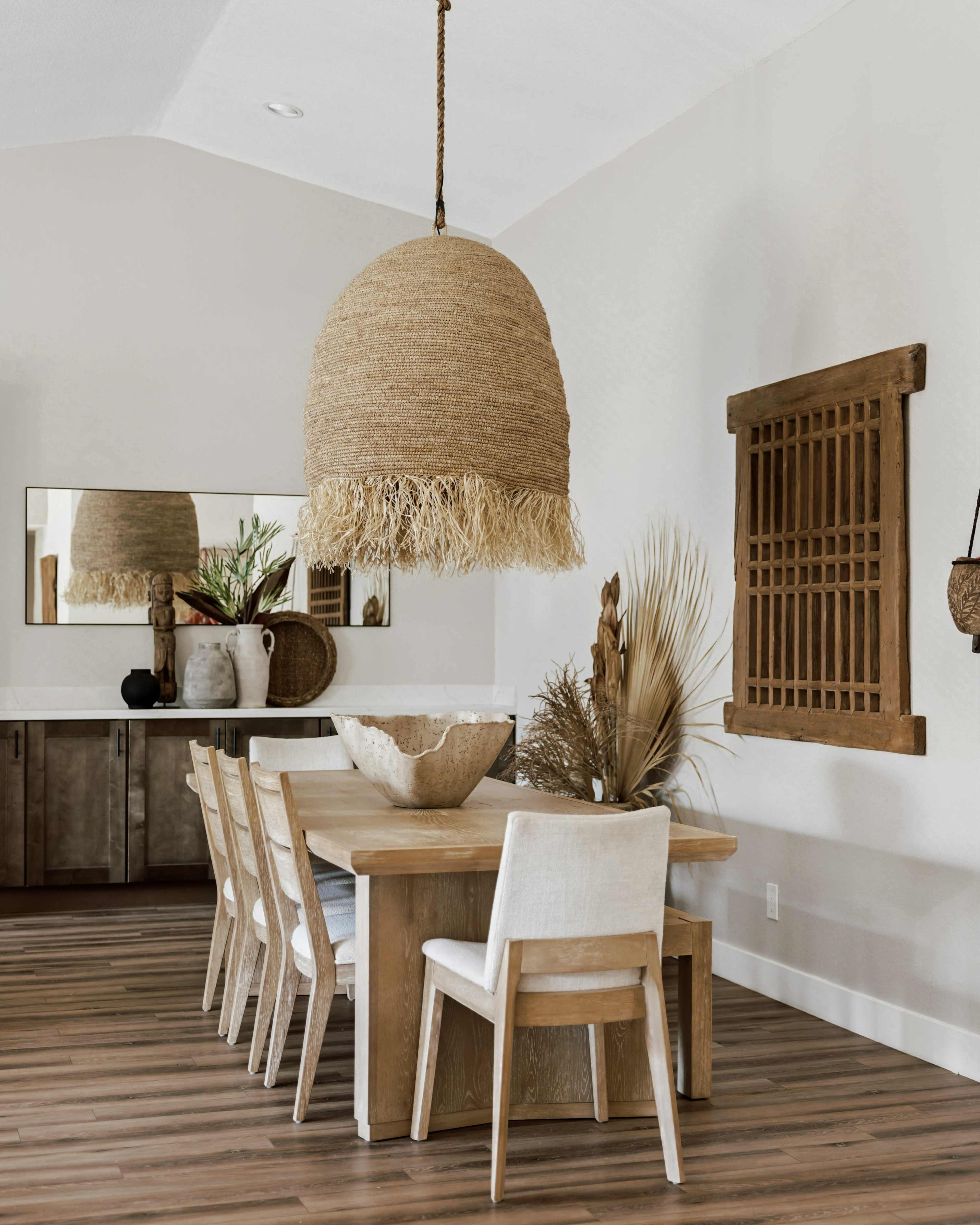 A dining area features a large woven pendant light above a wooden table surrounded by six white chairs, with decorative elements on the walls.