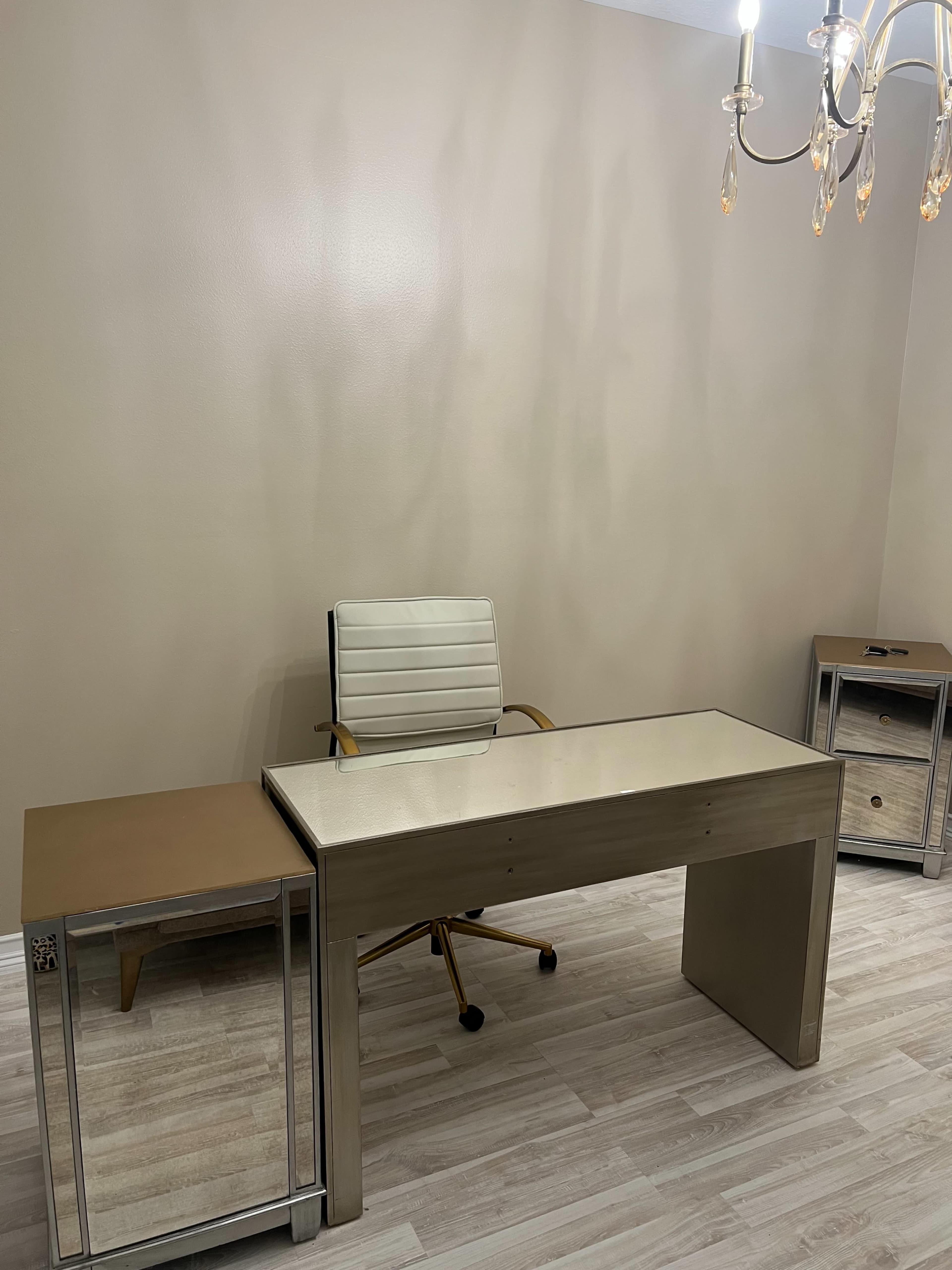A minimalist office space featuring a metallic desk, a striped office chair, and a matching nightstand, all set against a plain, light-colored wall.