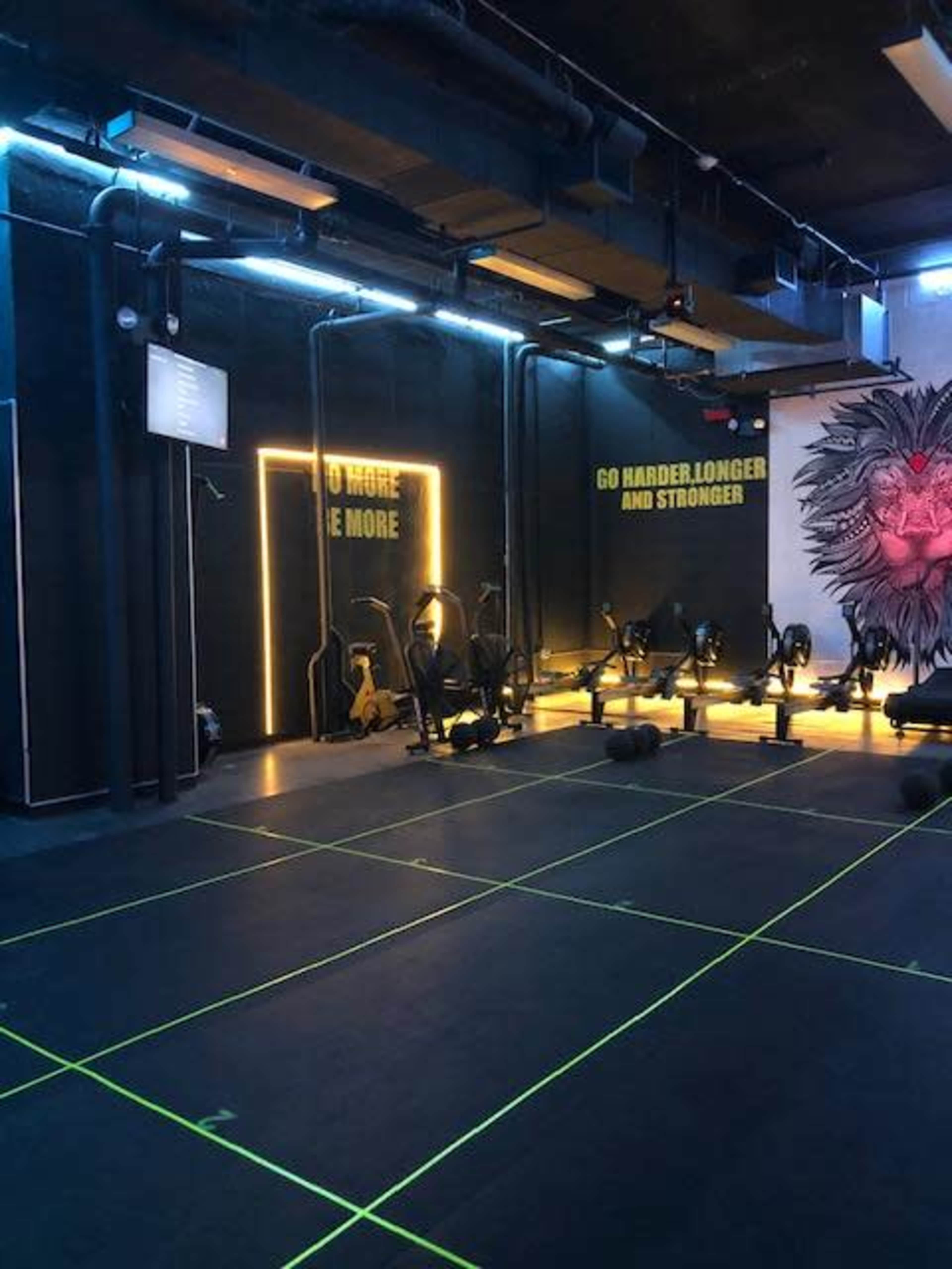The image shows a modern gym interior with exercise equipment, neon lighting, and motivational wall graphics.
