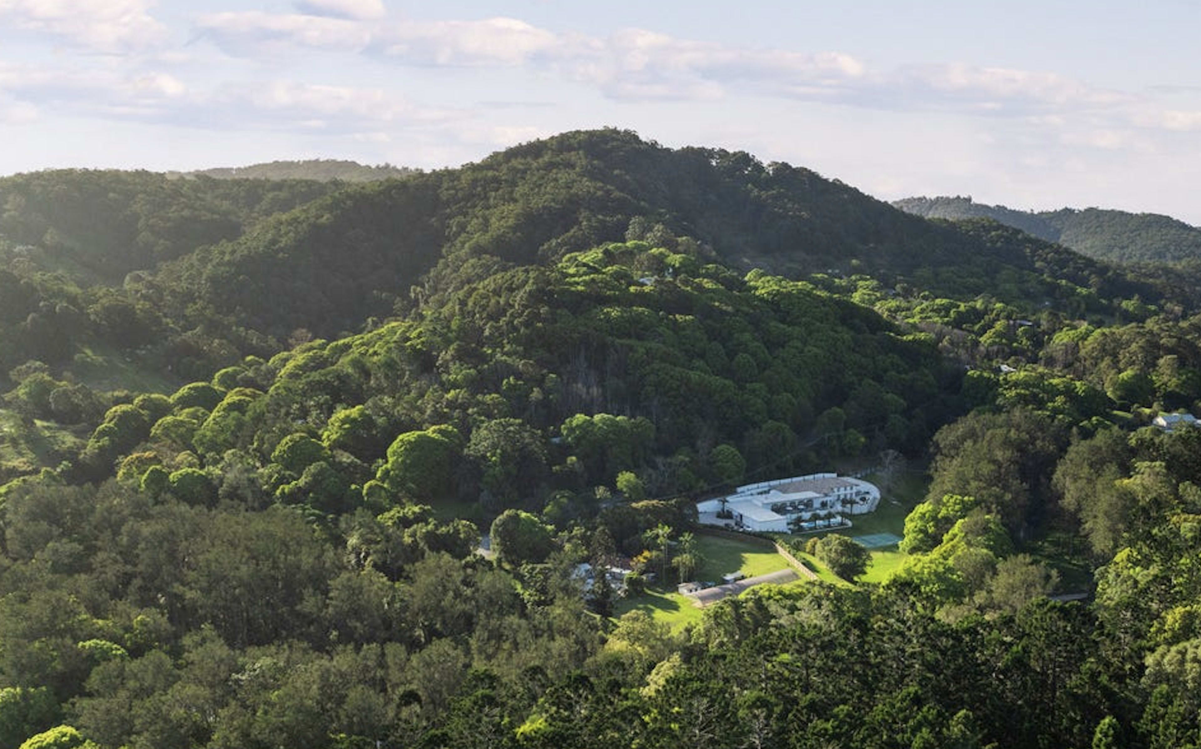 A sprawling white building is nestled among lush, green hills under a clear sky.