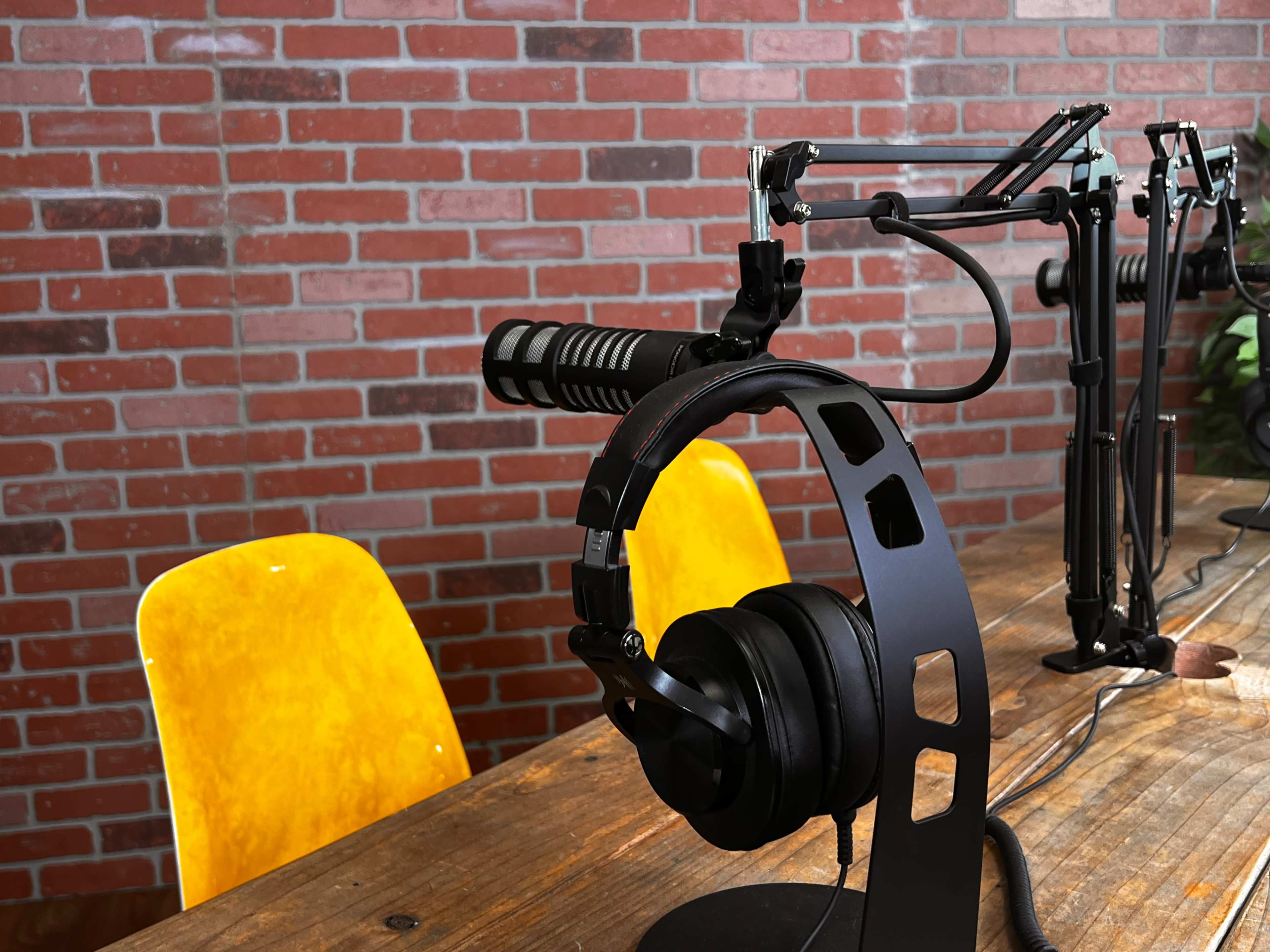 A microphone and headphones are positioned on a wooden table with yellow chairs and a brick wall in the background.