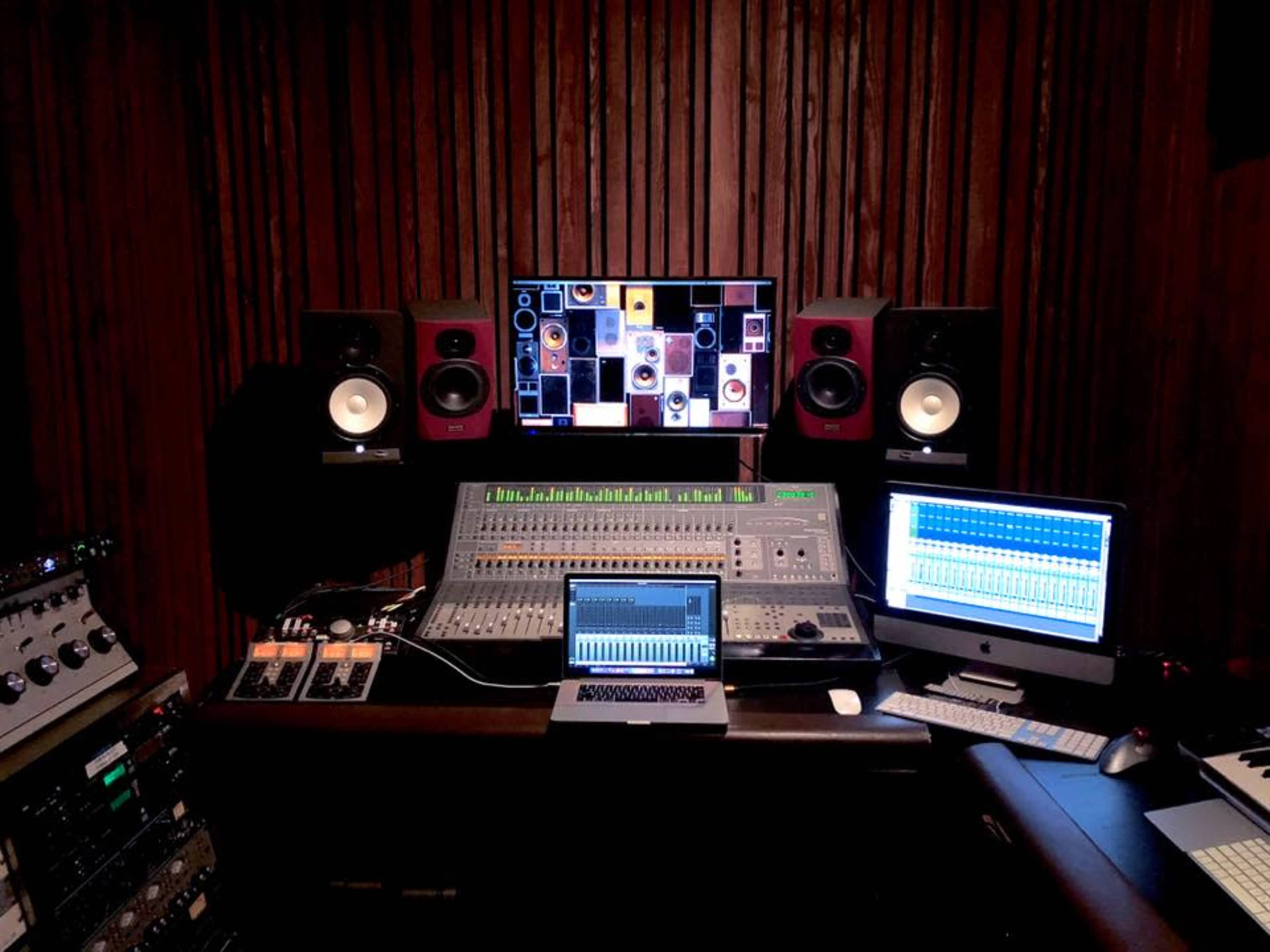 A sound mixing studio with multiple monitors, speakers, and a large audio mixer in a wooden-paneled environment.