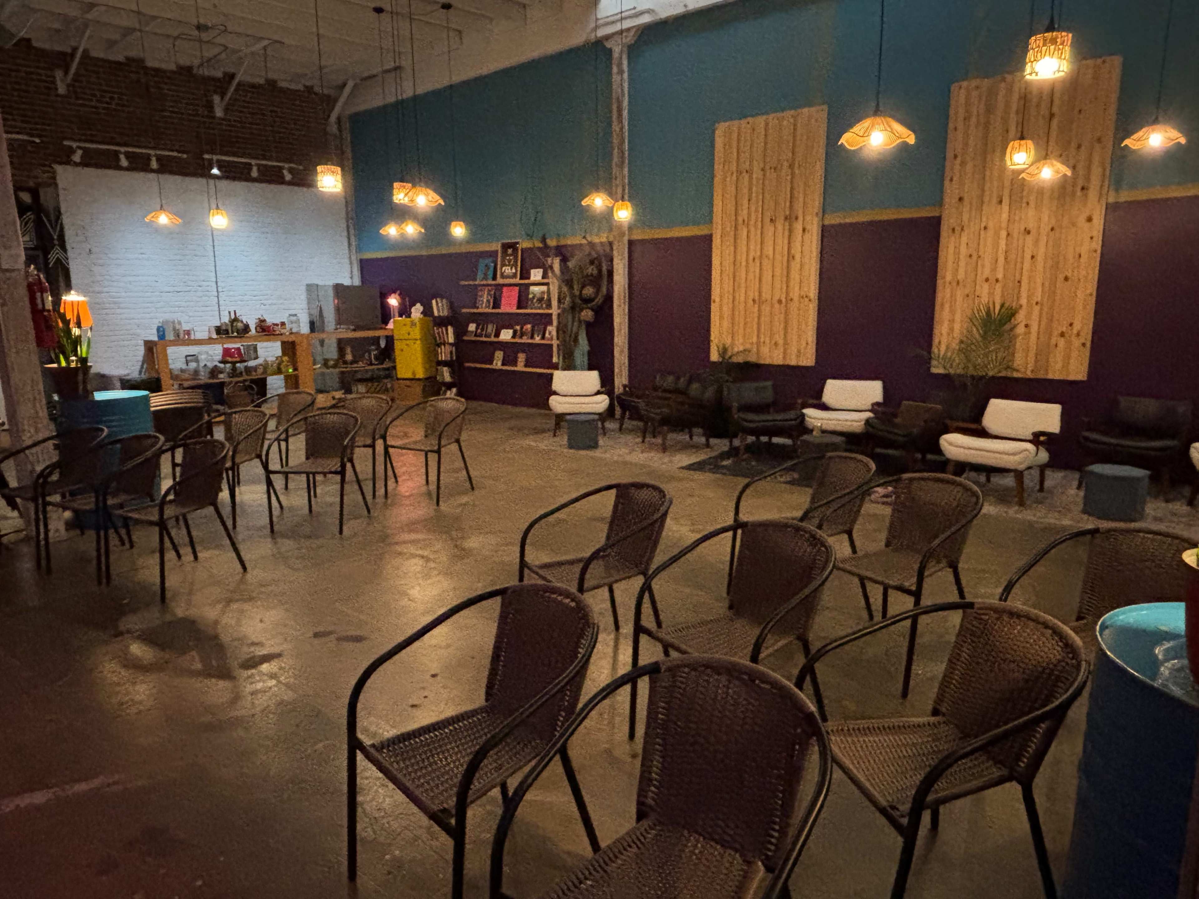 The image shows a spacious, industrial-style room with several empty chairs arranged in rows, colorful walls, and decorative lighting fixtures hanging from the ceiling.