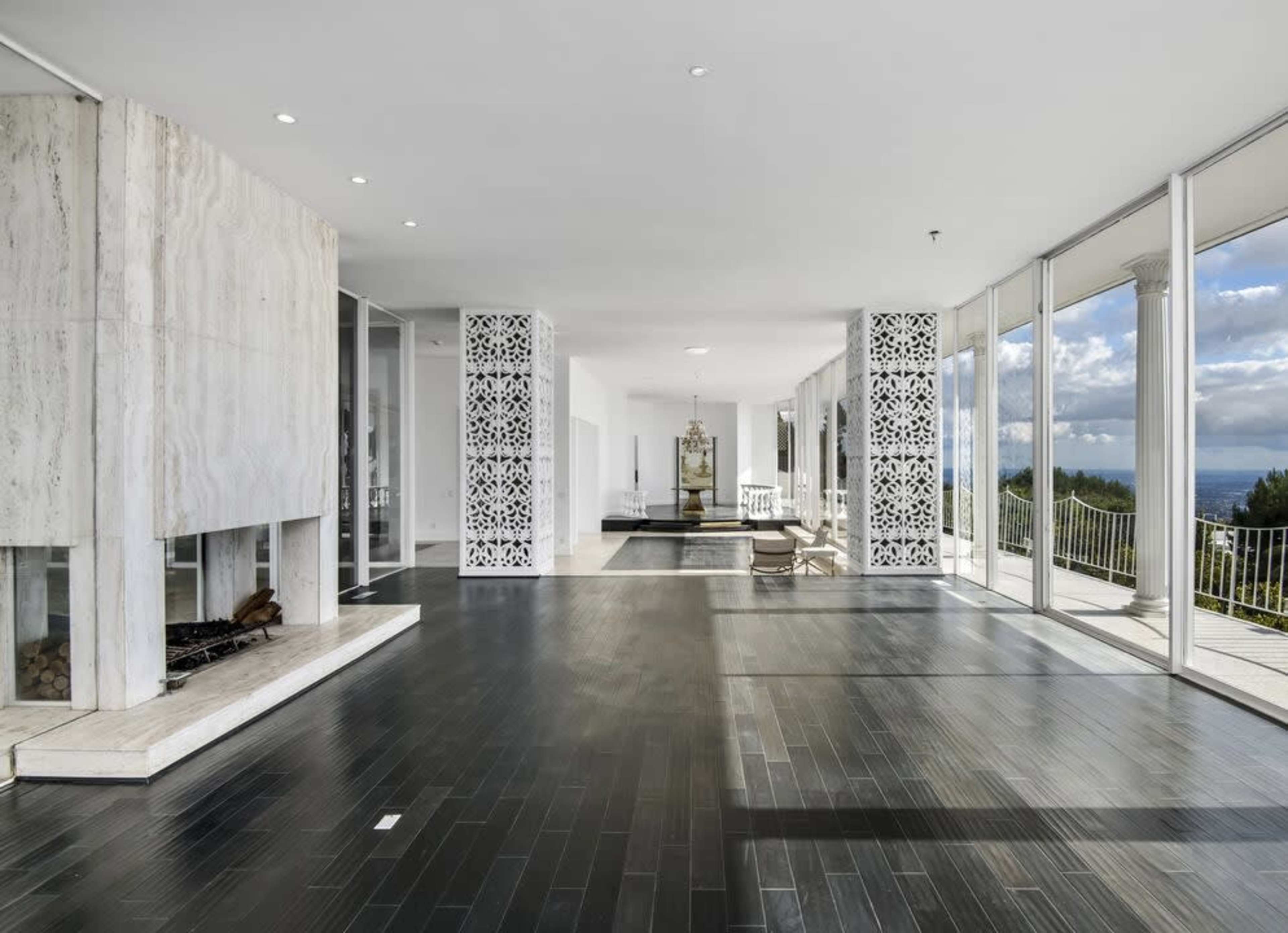 The image shows a spacious, modern interior with large glass windows, marble accents, and a wooden floor.