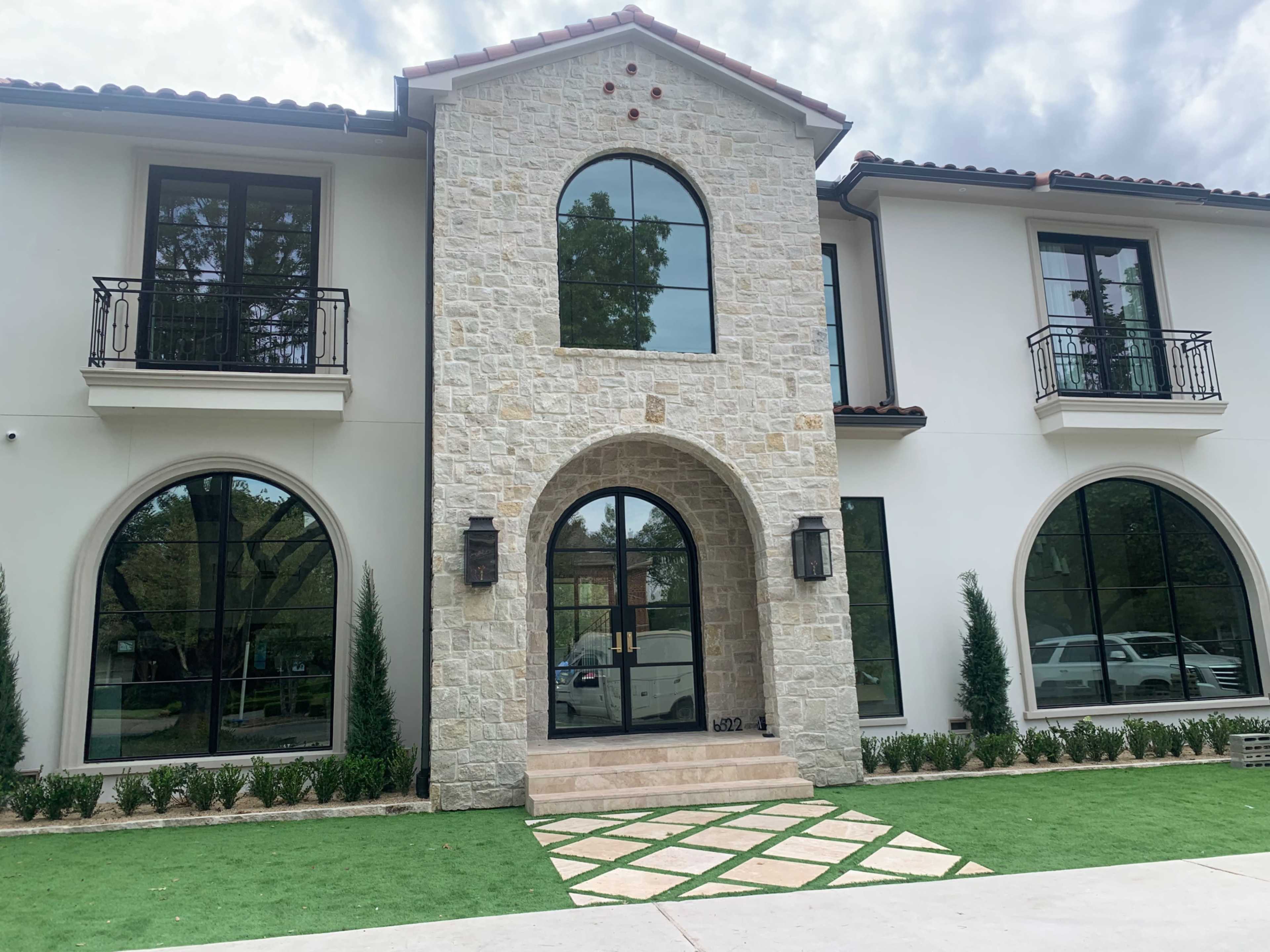 The image shows a two-story house featuring a stone facade, large arched windows, and a central arched entrance.