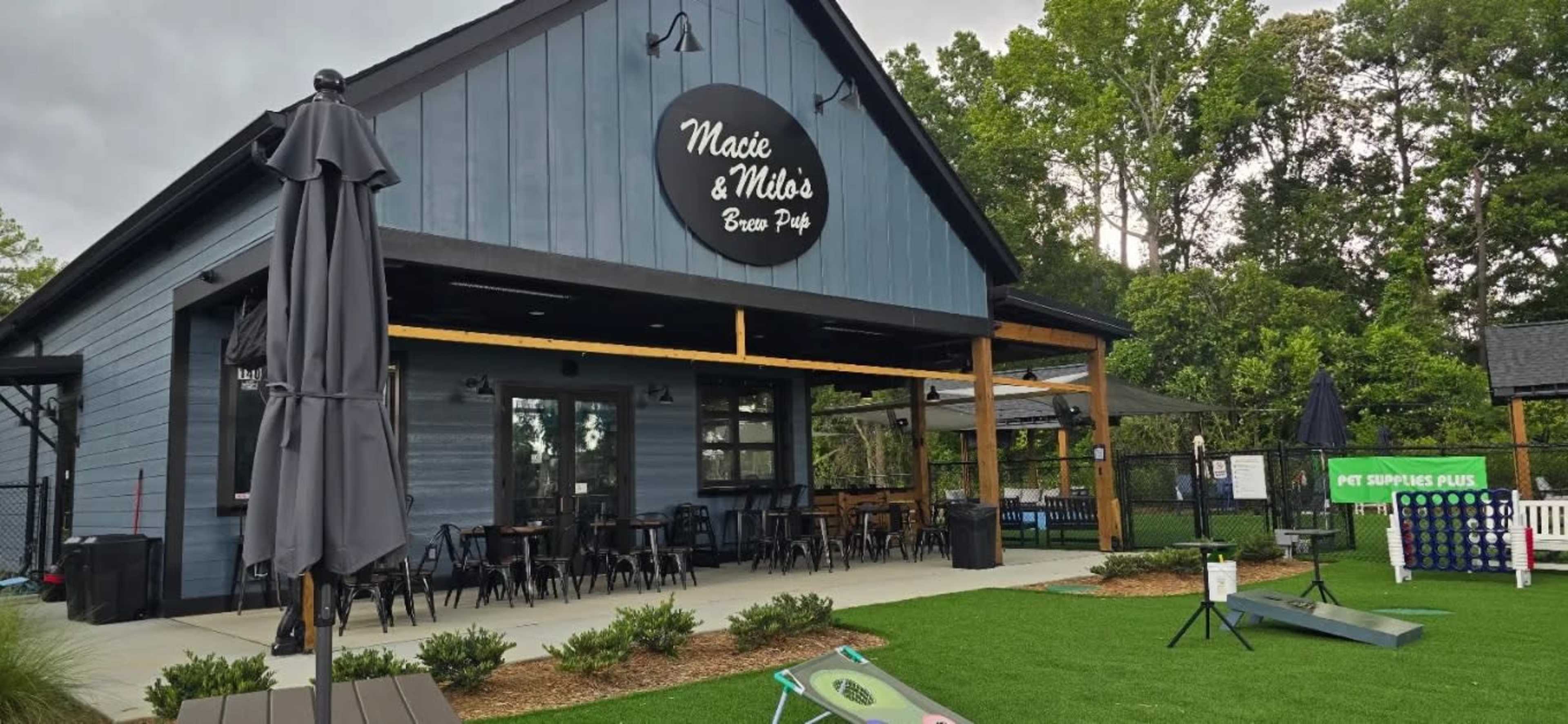 The image shows a blue wooden building with a sign that reads "Maxie & Milo's Brew Pub," surrounded by outdoor seating areas and a grassy landscape.