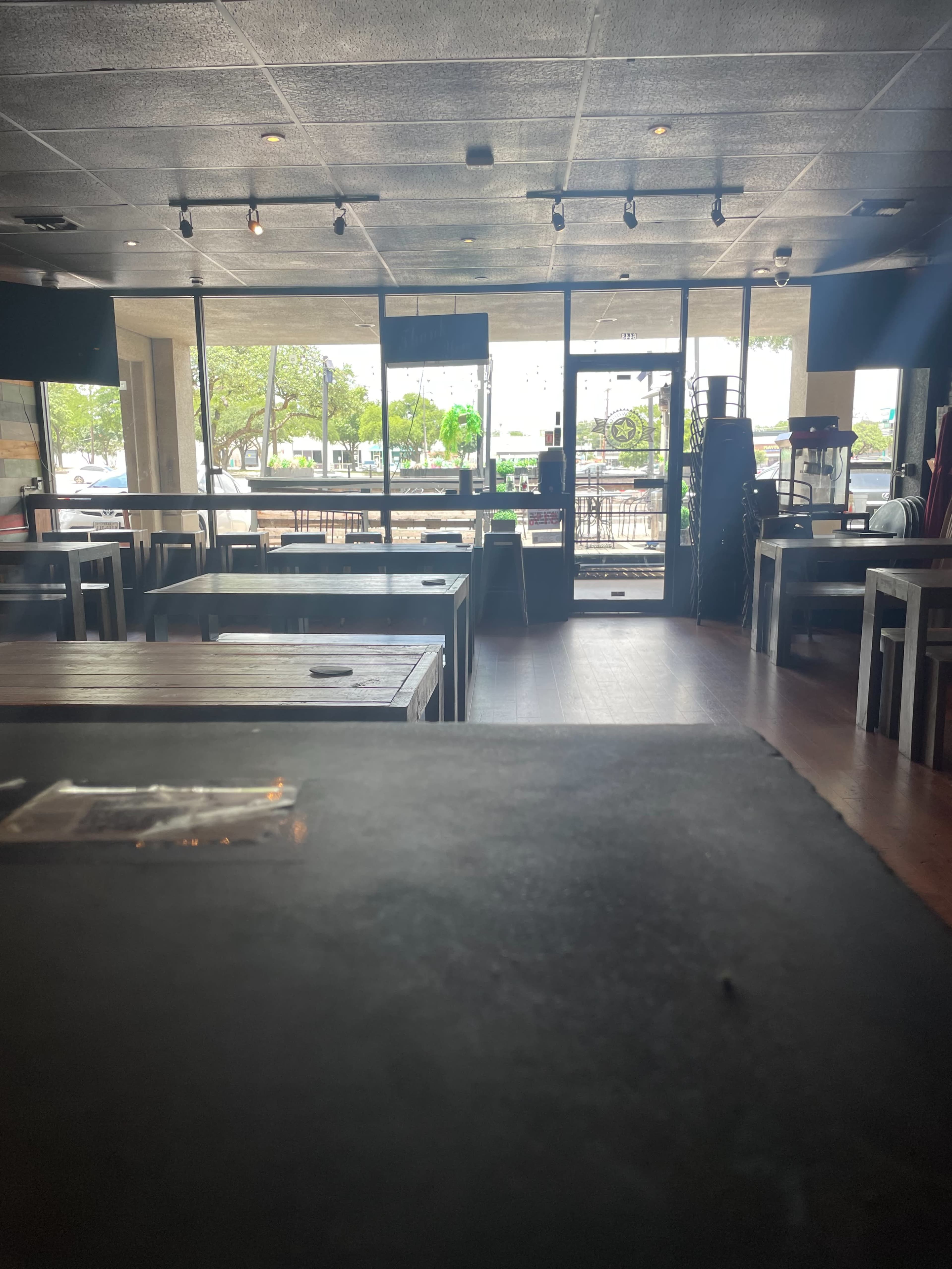 The interior of a restaurant with empty tables and large windows displaying an outdoor view.
