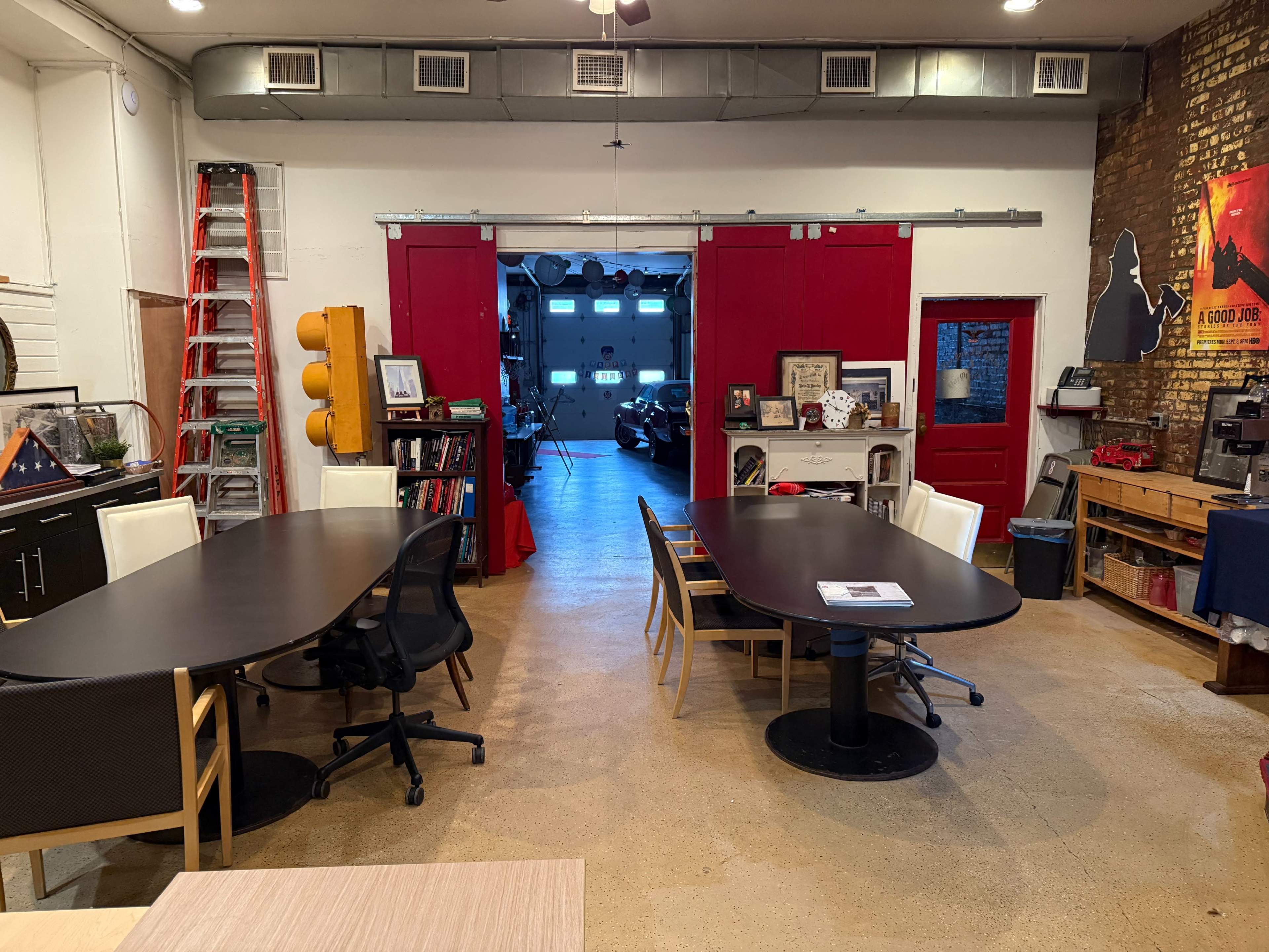 The image shows a spacious office area with two large tables, black chairs, a red door leading to another room, and various decor elements on the walls.
