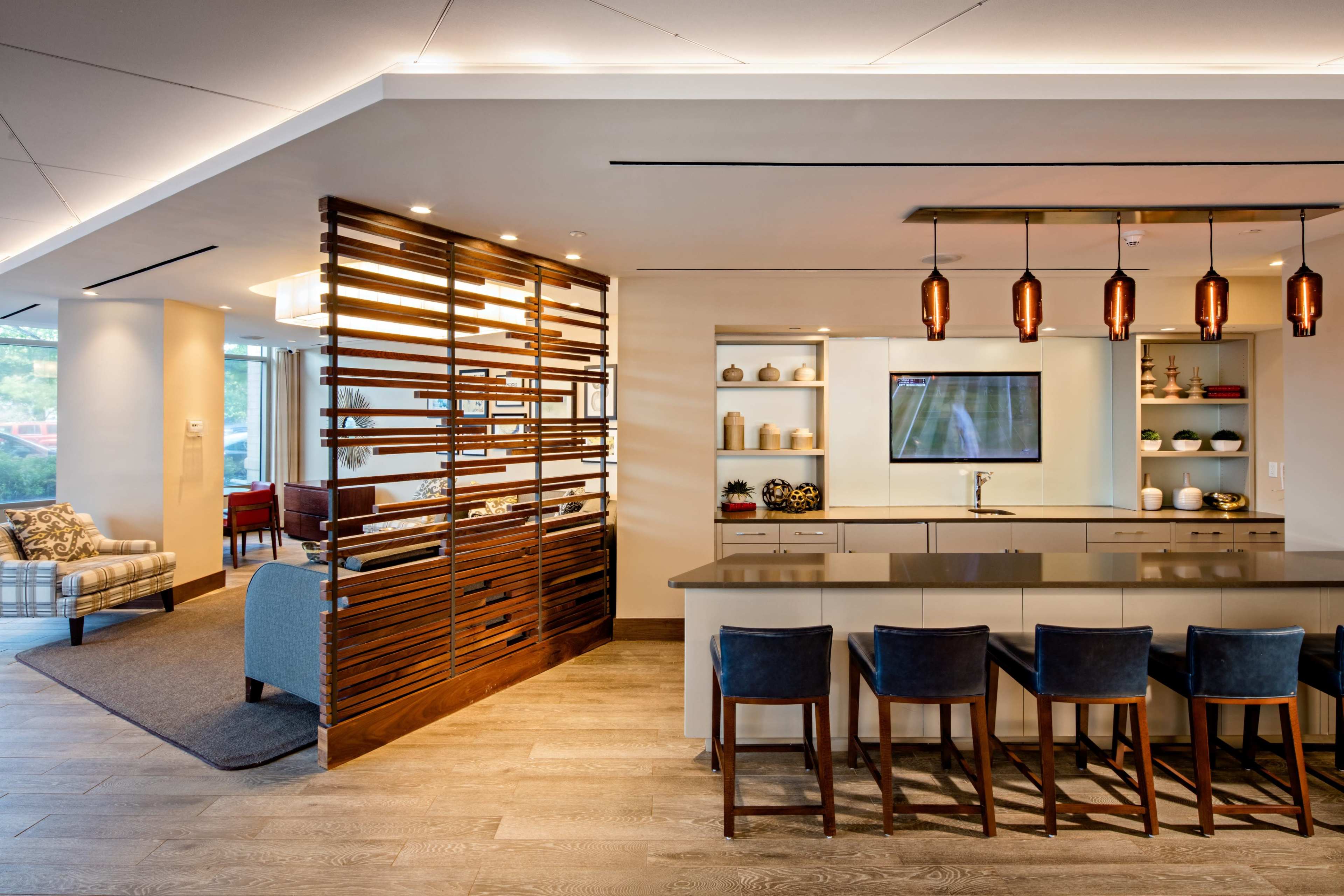 A modern kitchen and living area featuring a wooden partition, a central island with bar stools, and pendant lighting above.