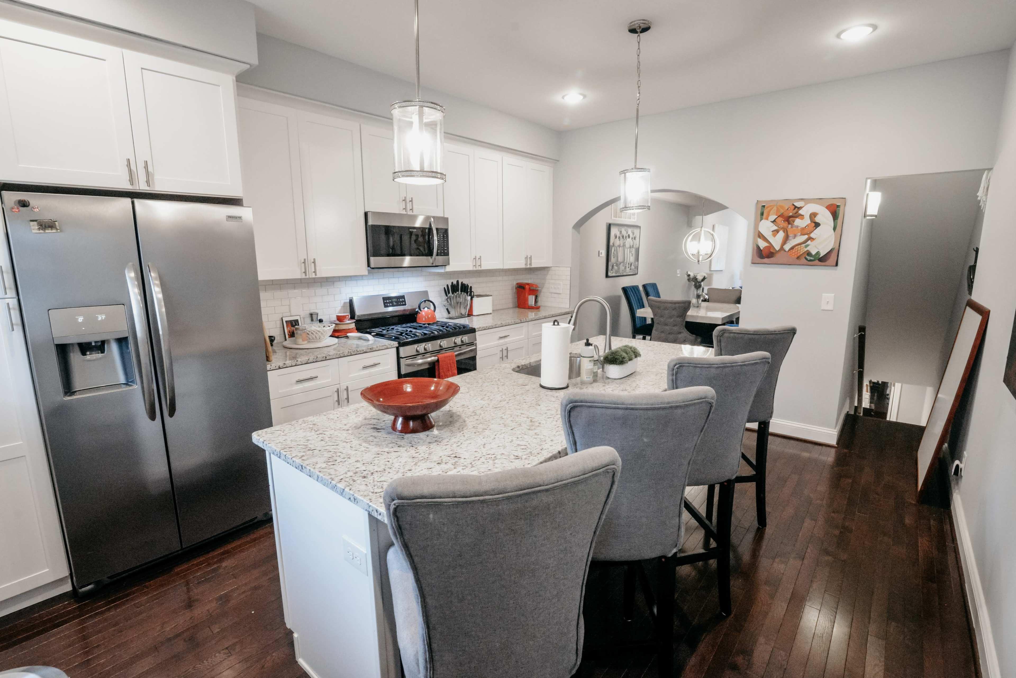The image shows a modern kitchen with white cabinets, a large island with gray bar stools, and stainless steel appliances.
