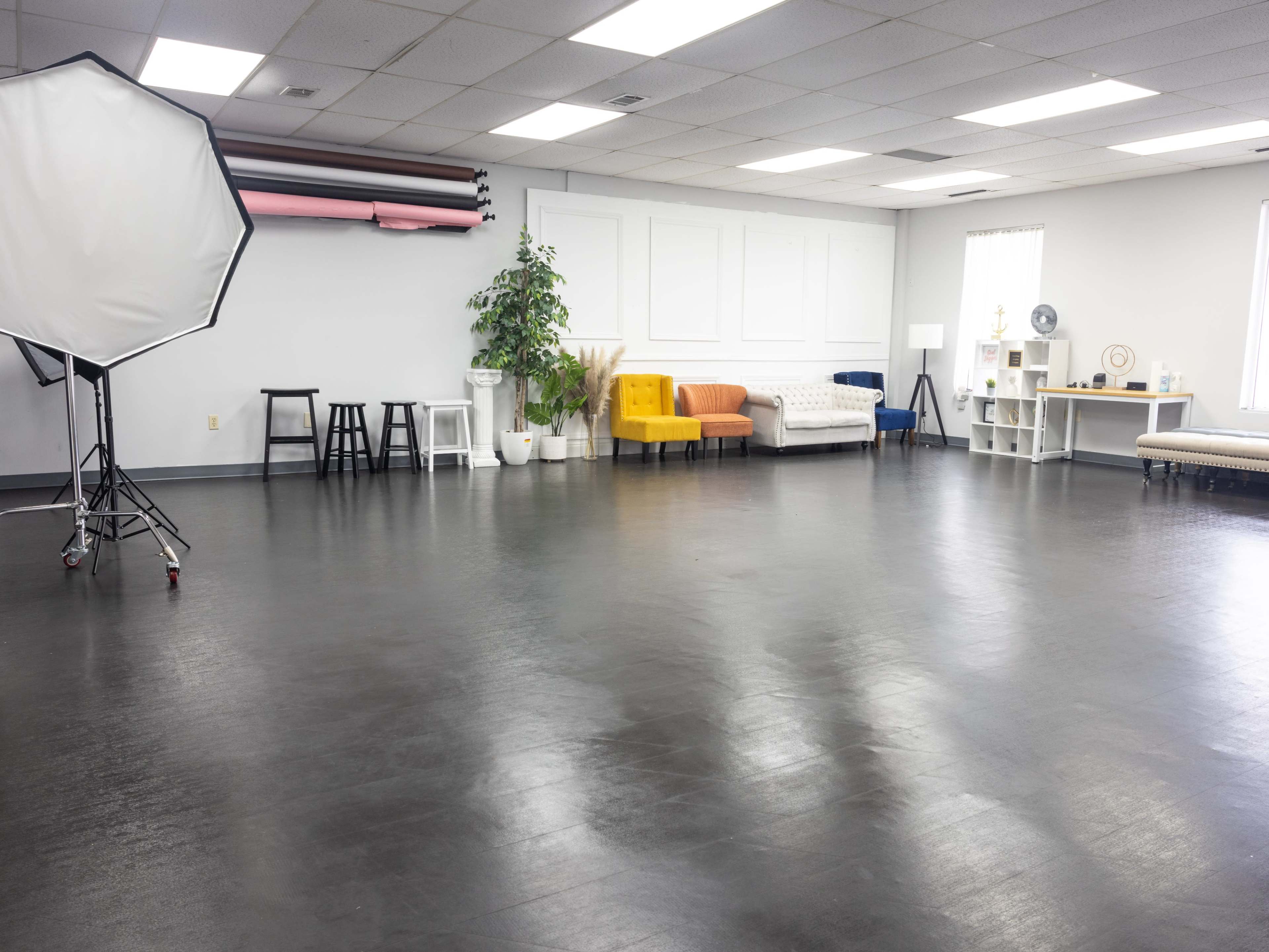 A spacious studio interior features a large window, a variety of seating options, and a backdrop setup.