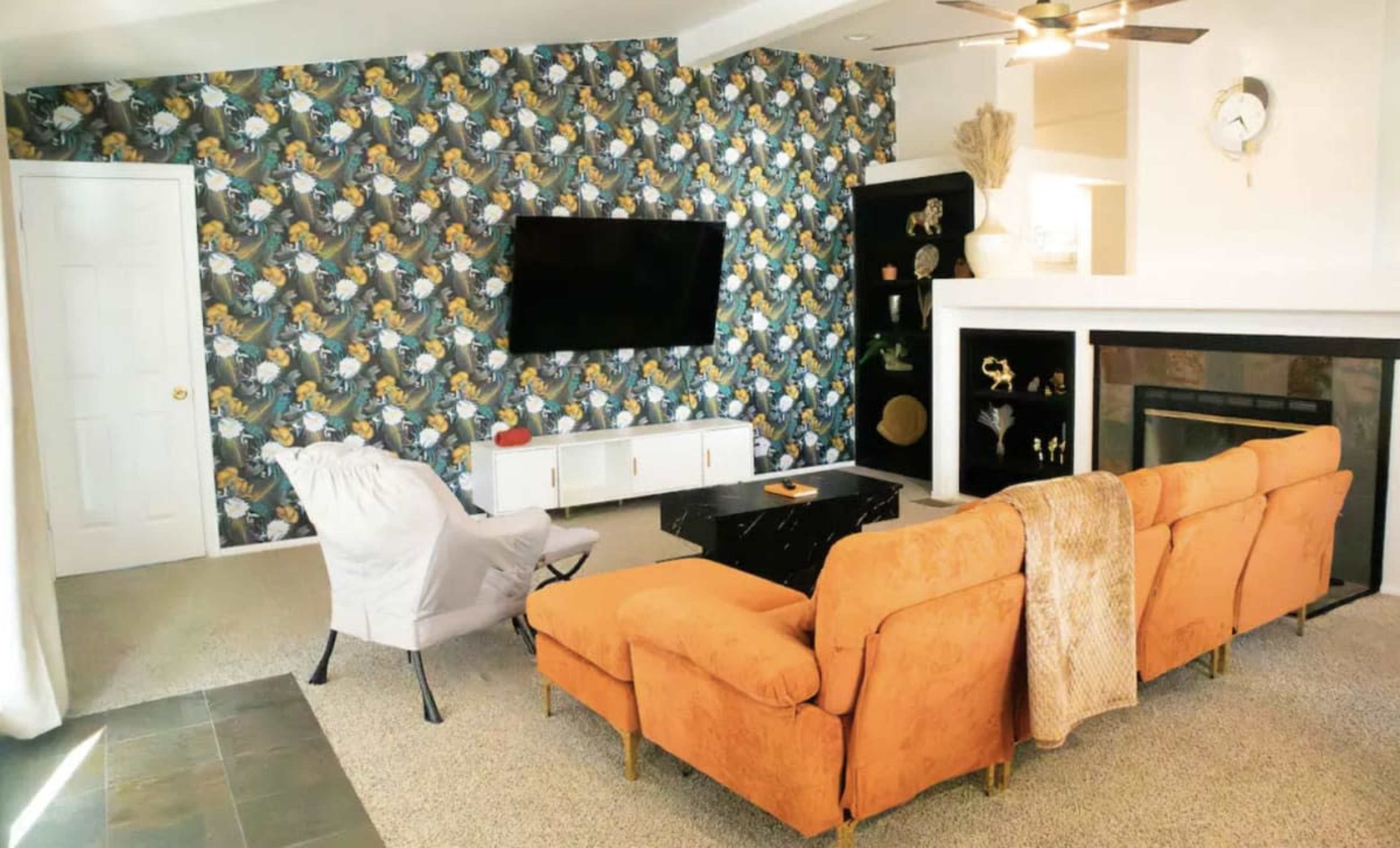 The living room features an orange sofa and a white chair, a black coffee table, a wall-mounted television, and a patterned wallpaper accent.