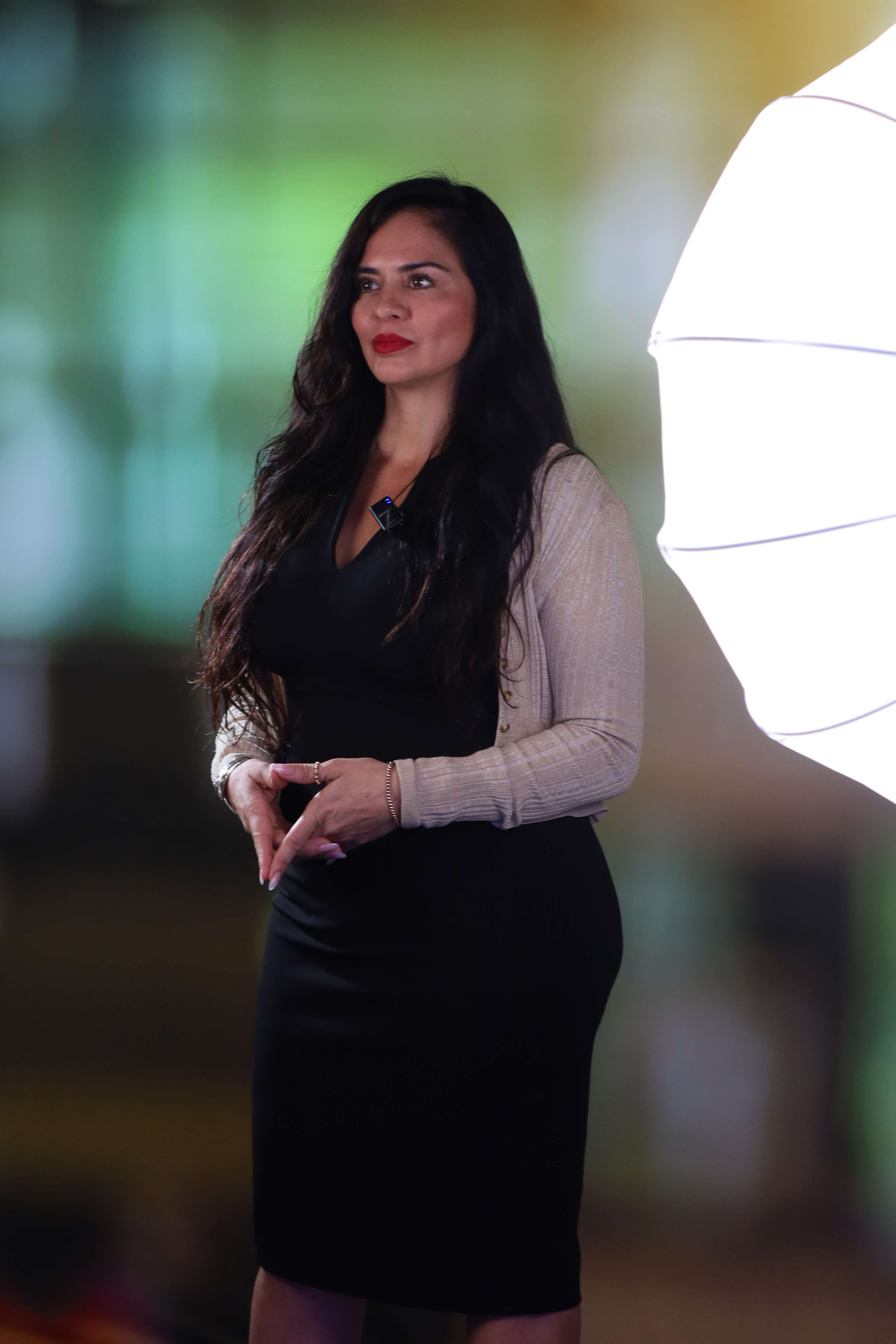 A woman in a black dress stands confidently beside a softbox light.