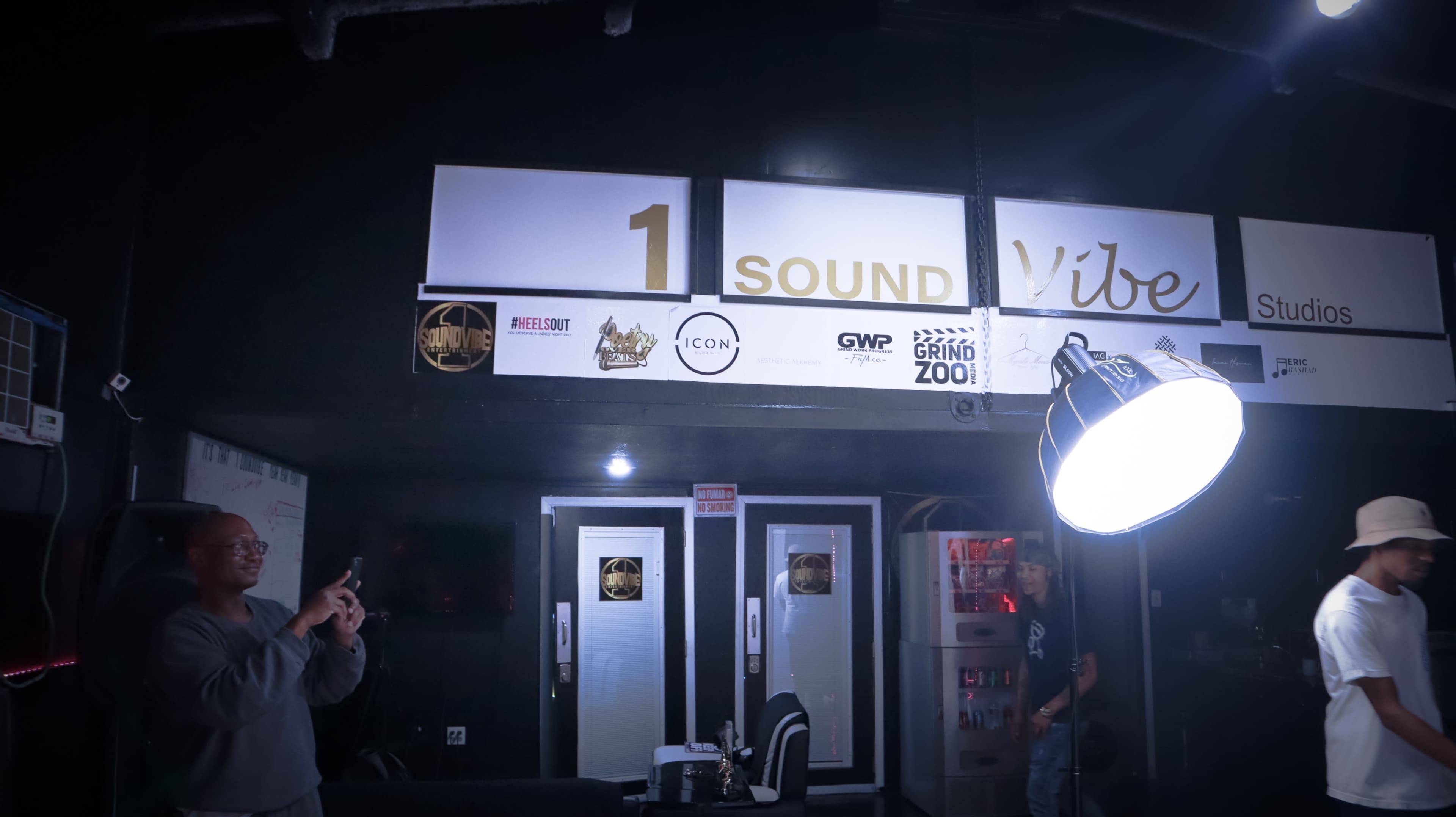 A dimly lit studio space with a prominent sign that reads "1 SOUND Vibe Studios" and two doors on the front.