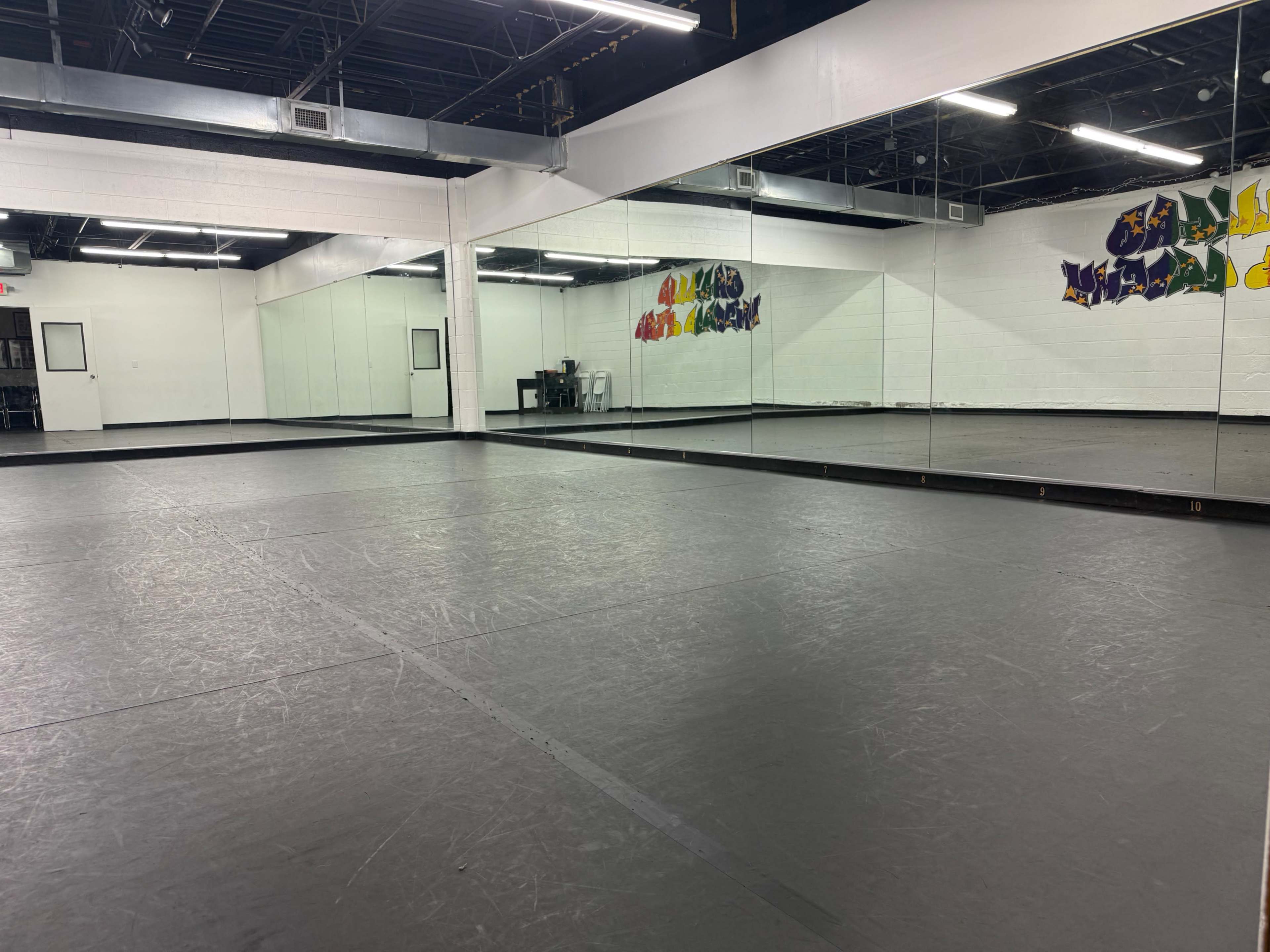 The image shows a spacious dance studio with mirrors lining one wall and a black floor.