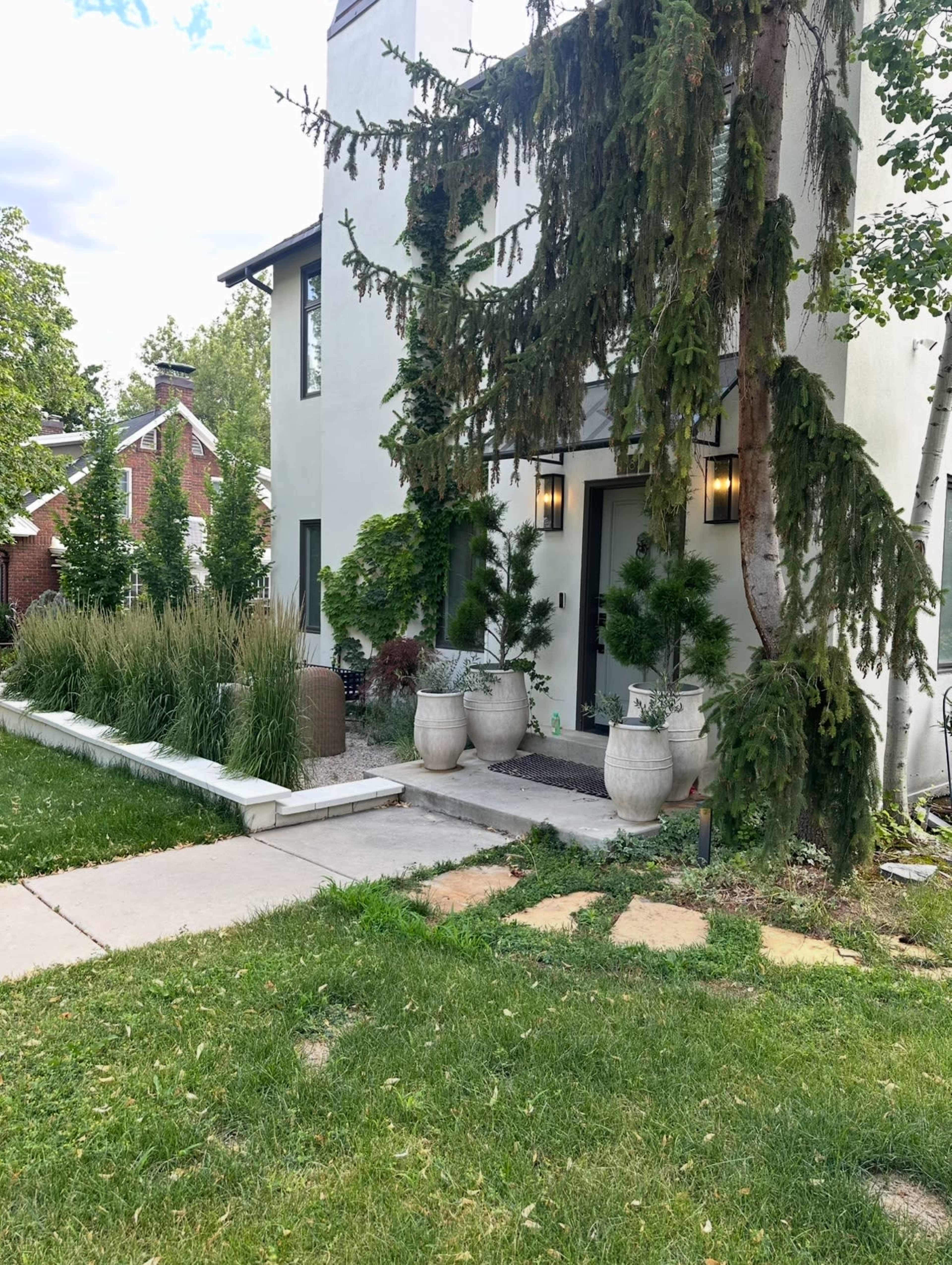 The image shows a modern home with a landscaped front yard featuring tall grasses and potted plants near the entrance.