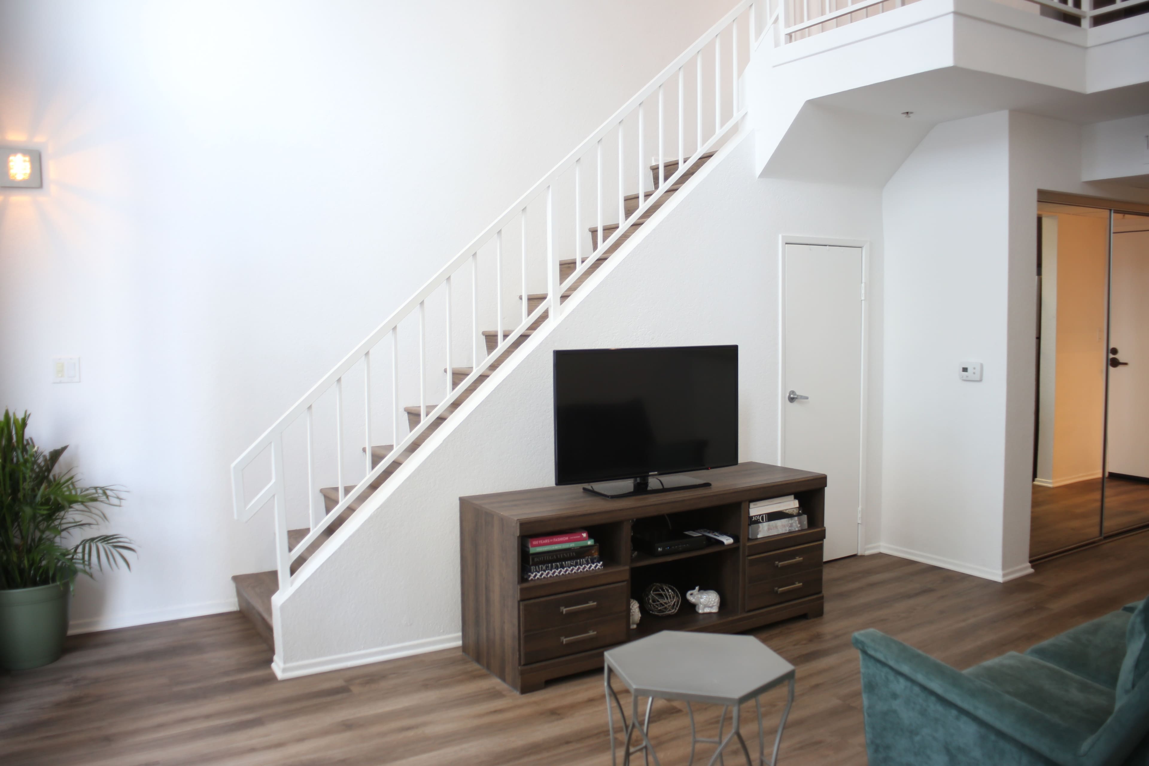 A living room with a television stand and a flat-screen TV positioned against a wall near a staircase leading to an upper level.