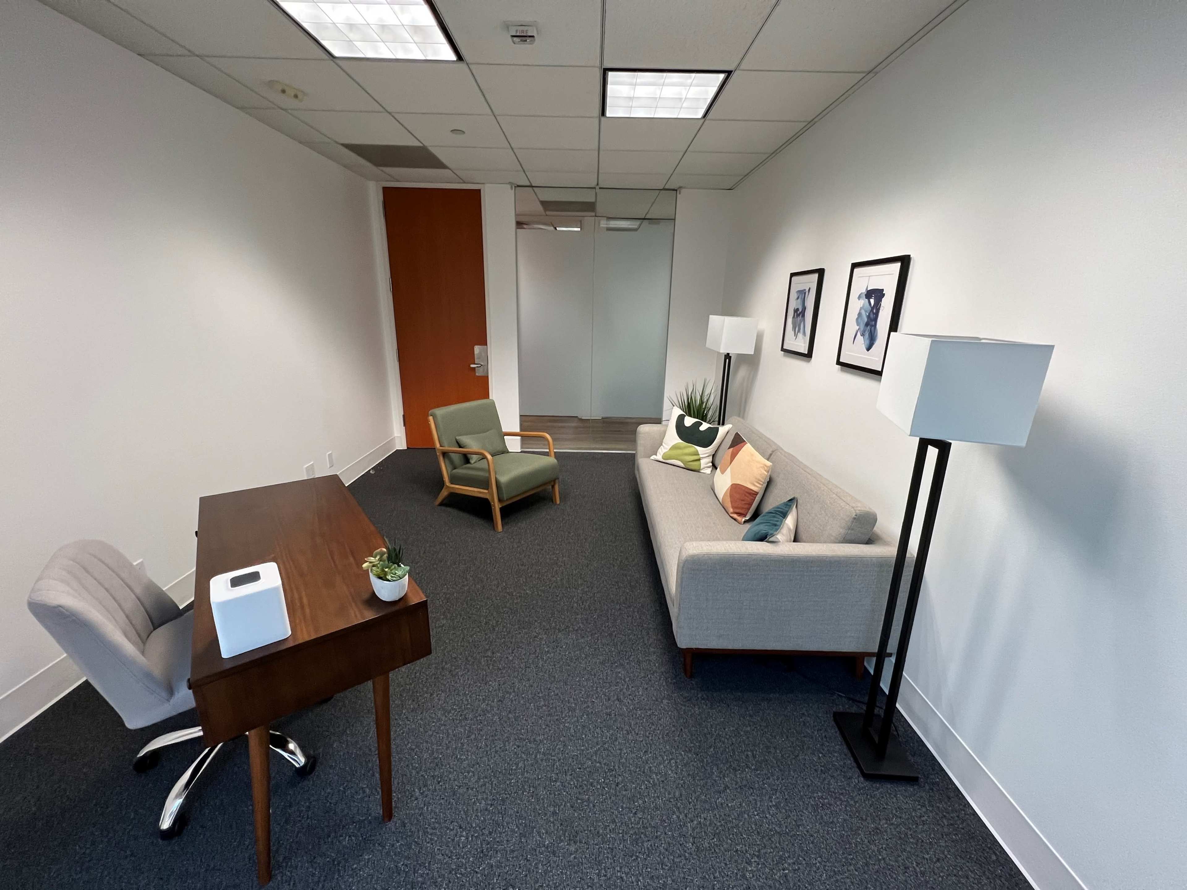 A minimally furnished office space featuring a desk with a chair, a sofa, and two lamps.