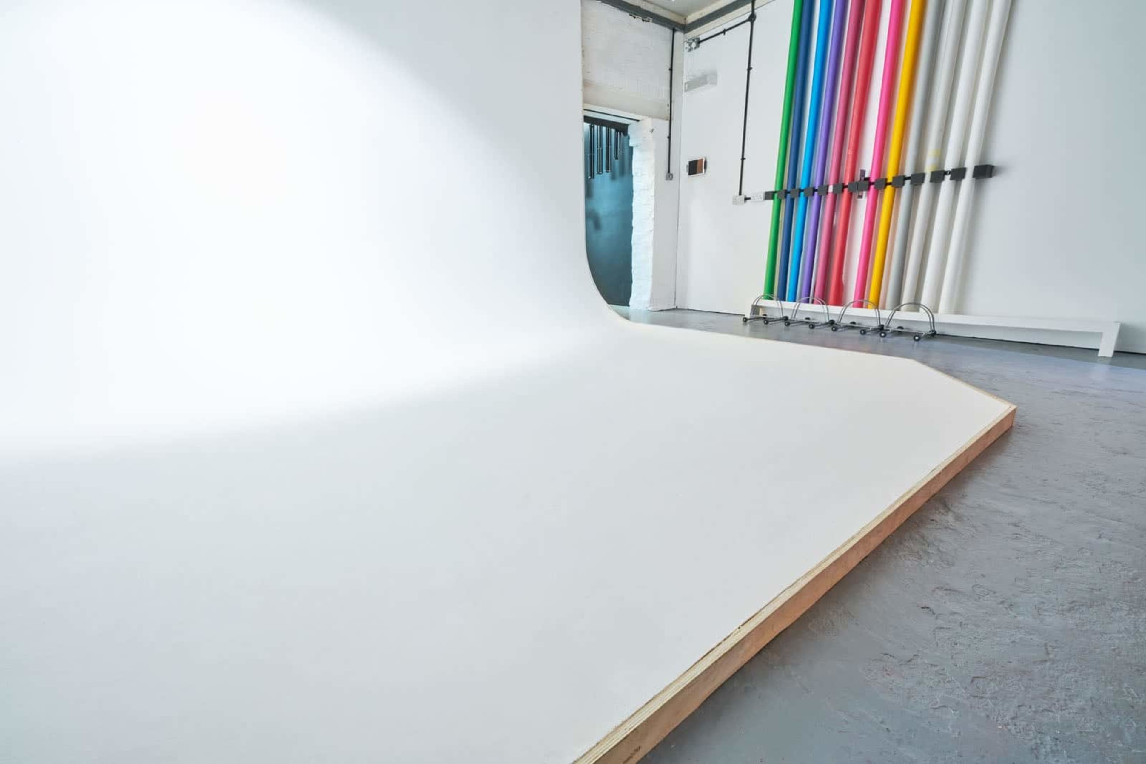 A photography studio featuring a white seamless backdrop and a colorful array of vertical pipes.