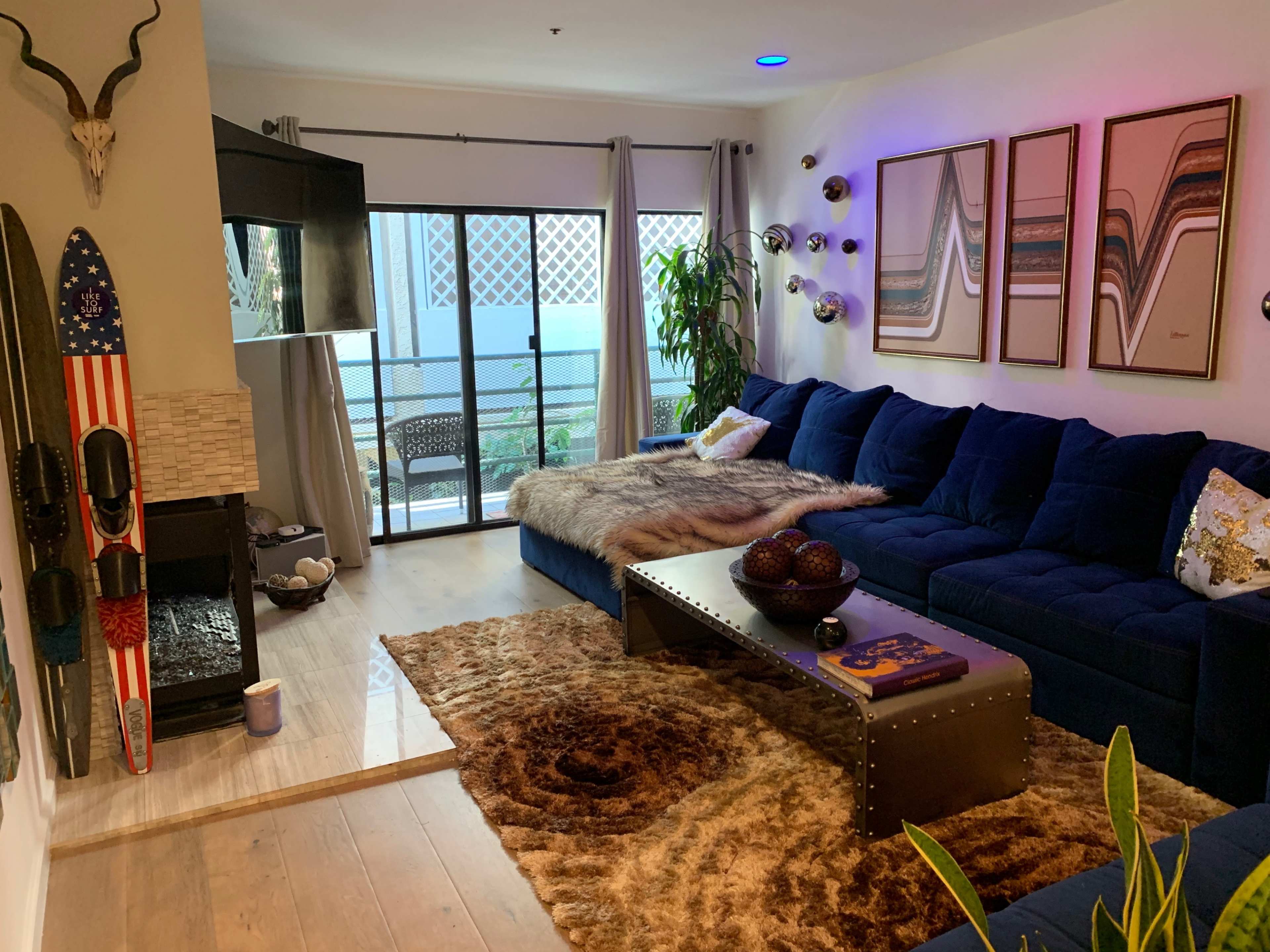 The room features a modern living space with a blue sectional sofa, a coffee table, and large windows that open to a balcony.