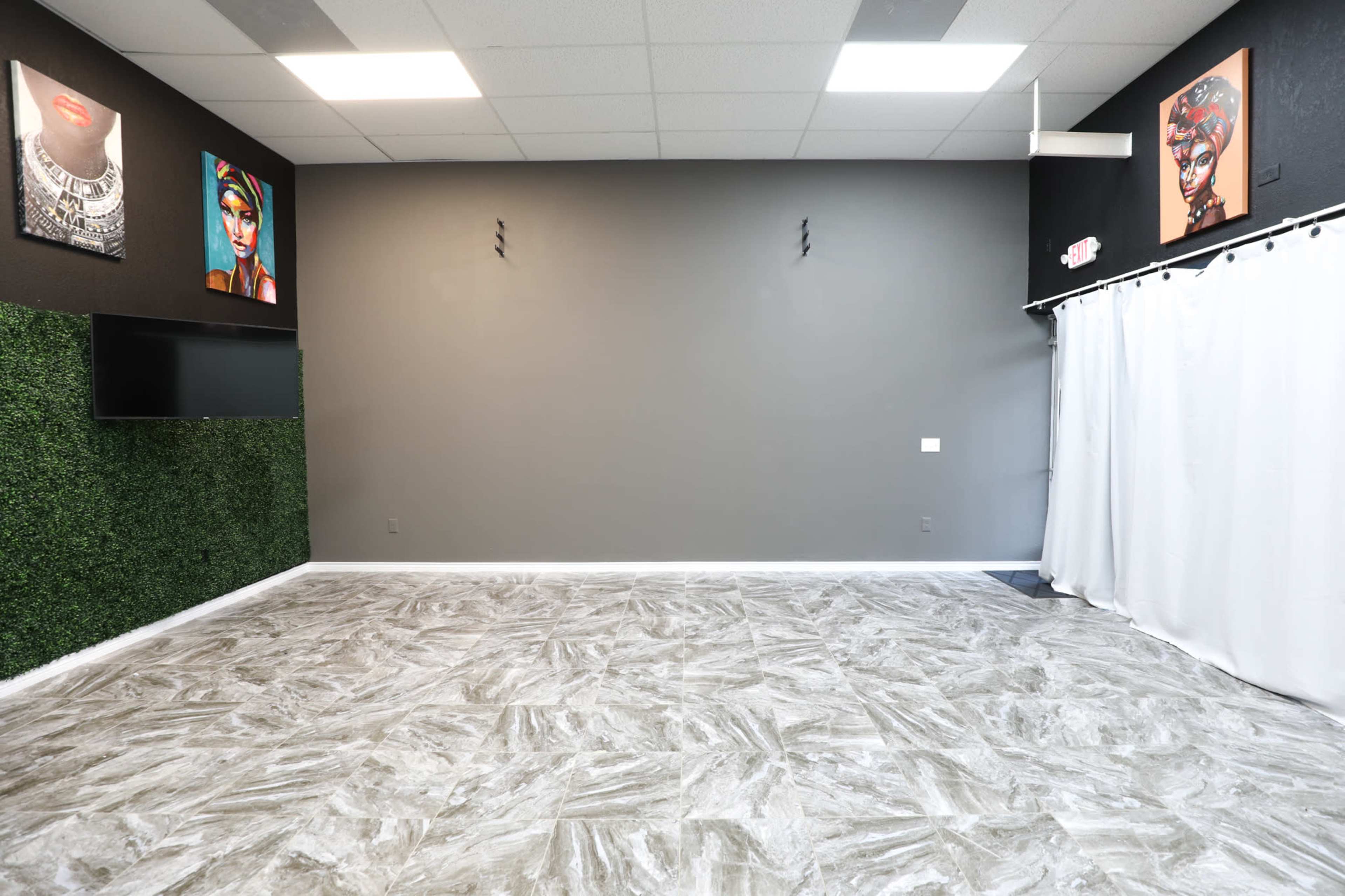 A spacious room with gray walls, a decorative artificial grass section, a television mounted on the wall, and two framed artworks displayed on the walls.