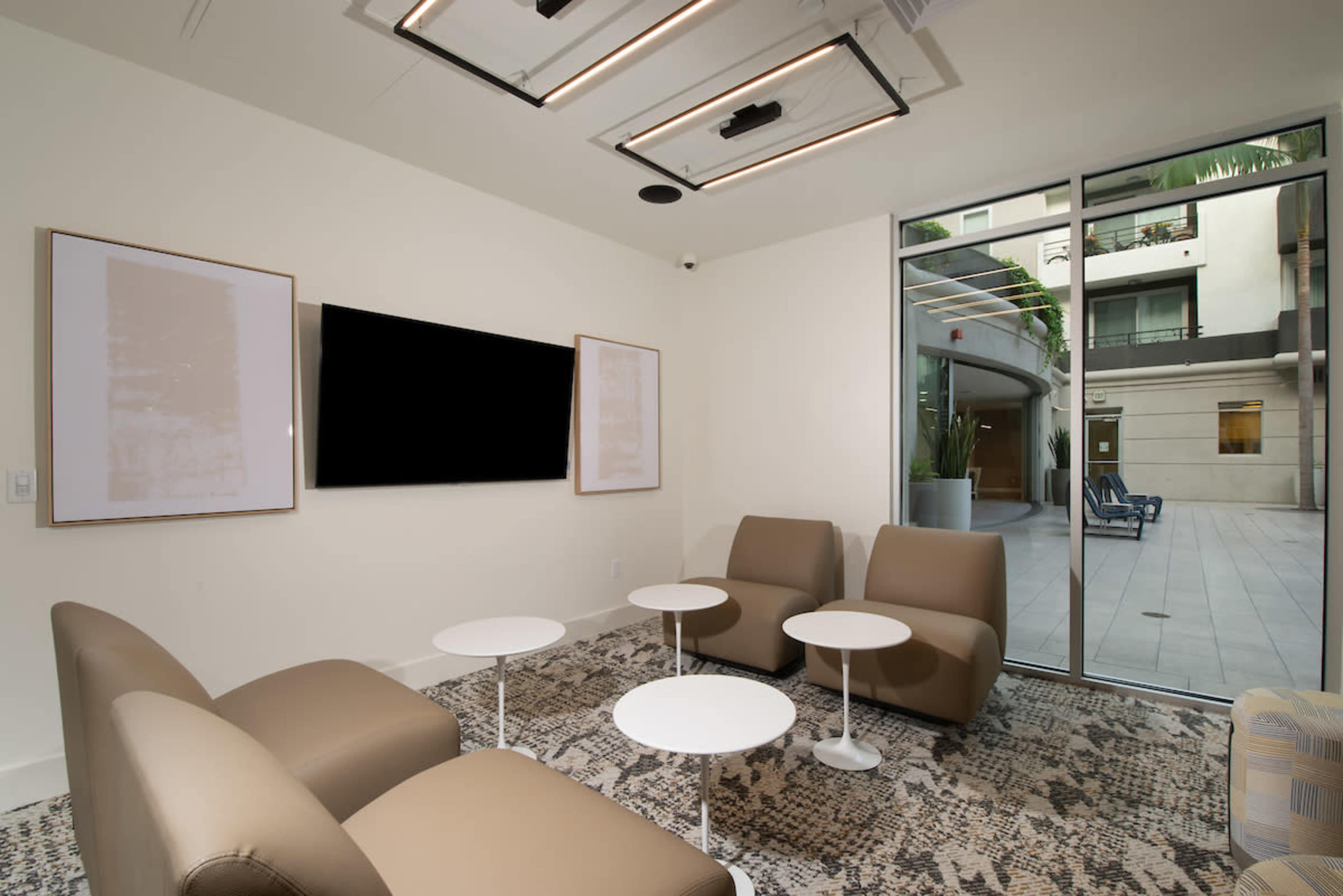 A modern lounge area featuring beige chairs, white tables, and a large window overlooking an exterior space.