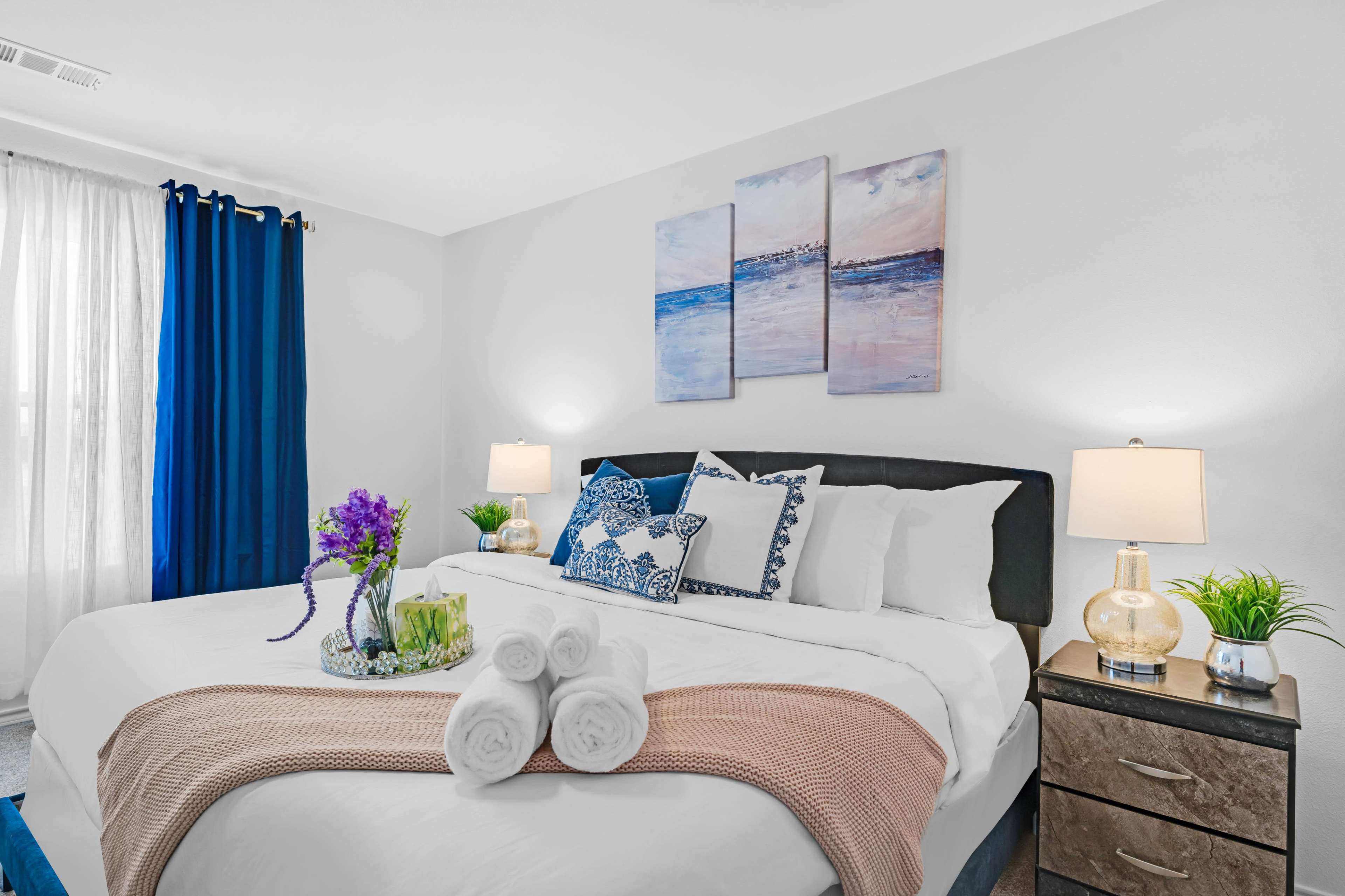 A neatly arranged bedroom featuring a large bed with decorative pillows, bedside lamps, and a small vase of flowers on the bed.