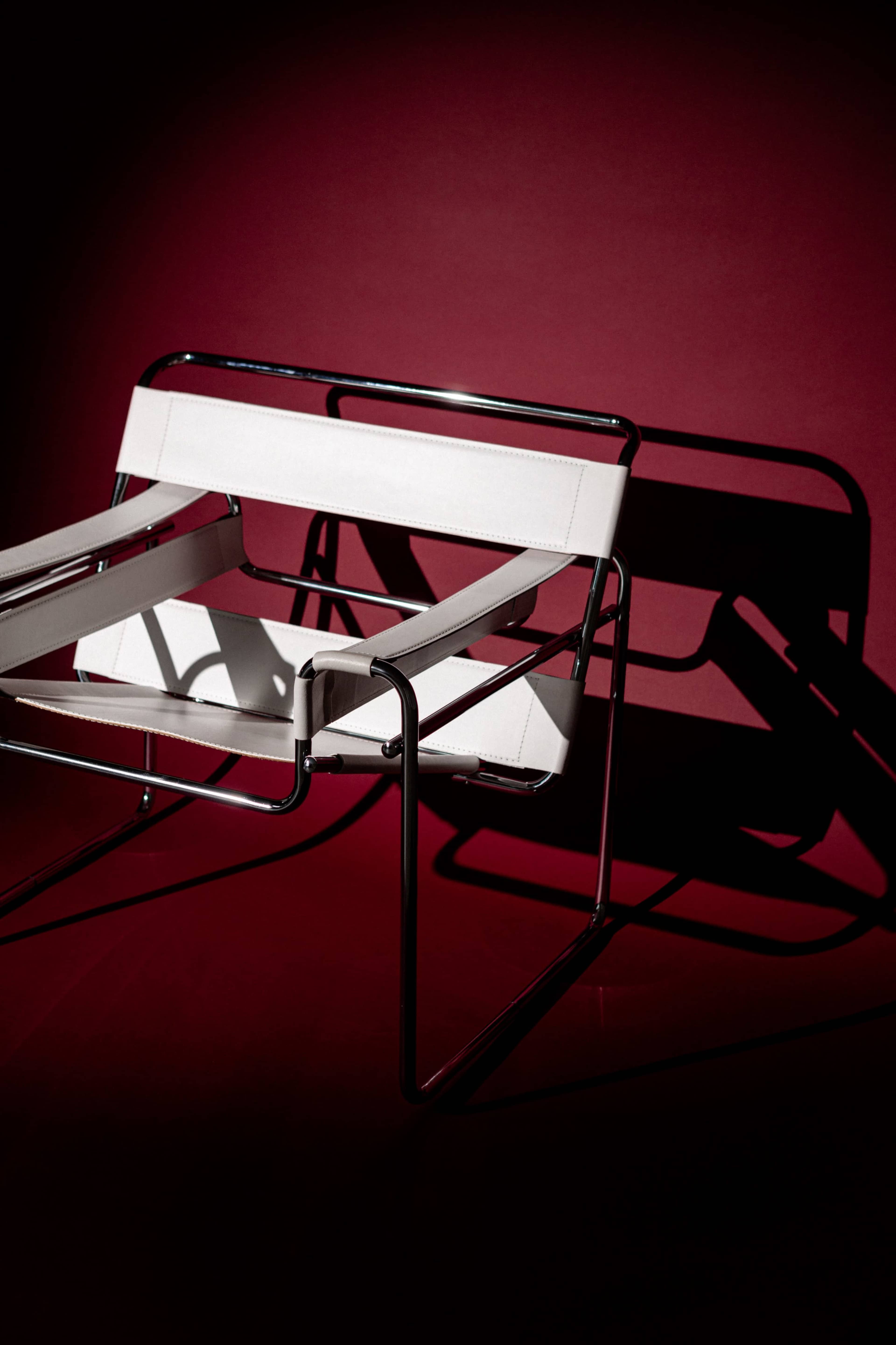 A white chair with a minimalist design casts a shadow against a deep red background.