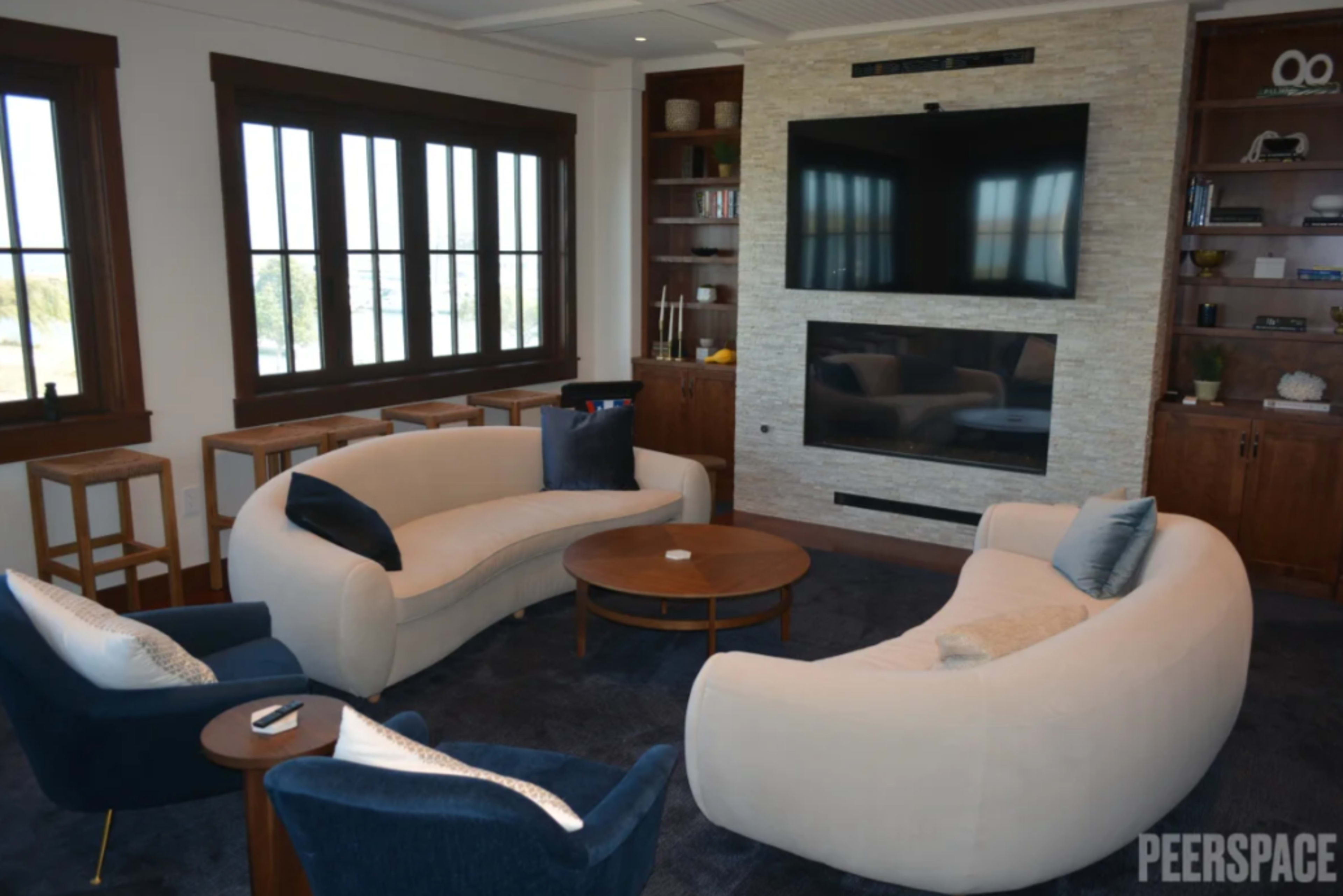 The image shows a modern living room with two curved sofas, a round coffee table, and a large wall-mounted television.