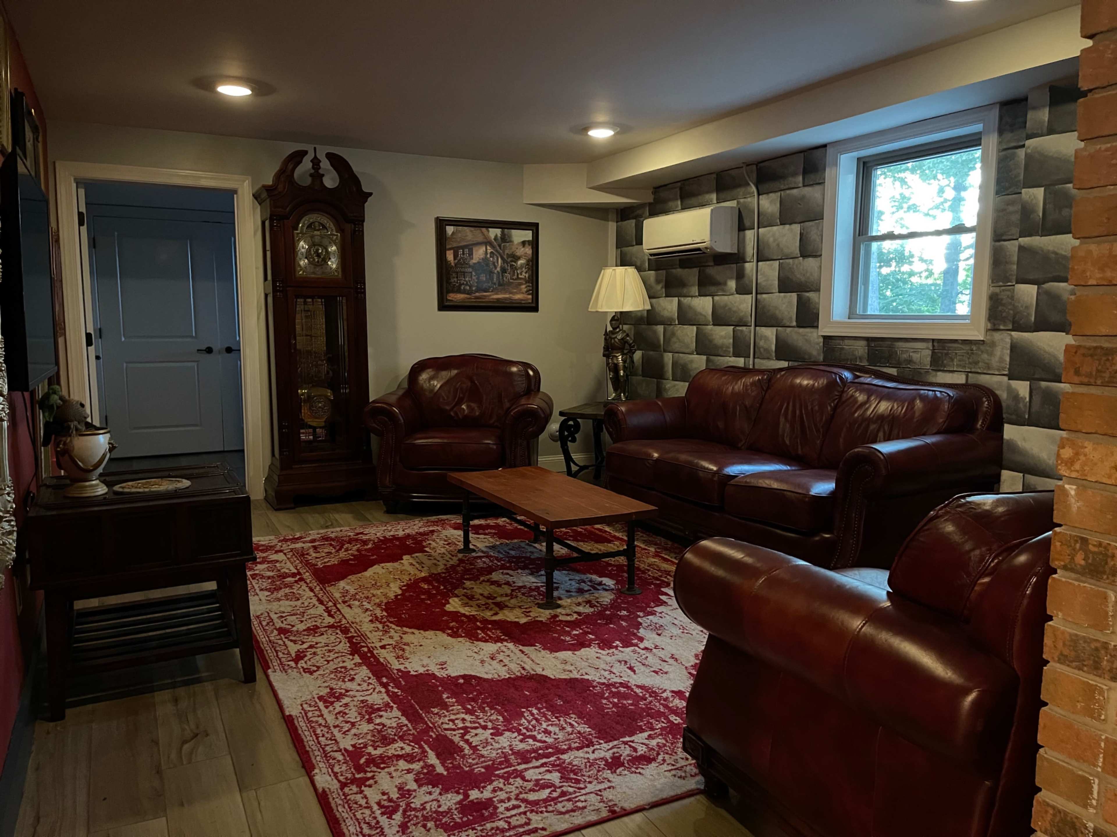 The image shows a living room with leather sofas, a wooden coffee table, a decorative rug, and a large wall clock against a backdrop of textured wallpaper.