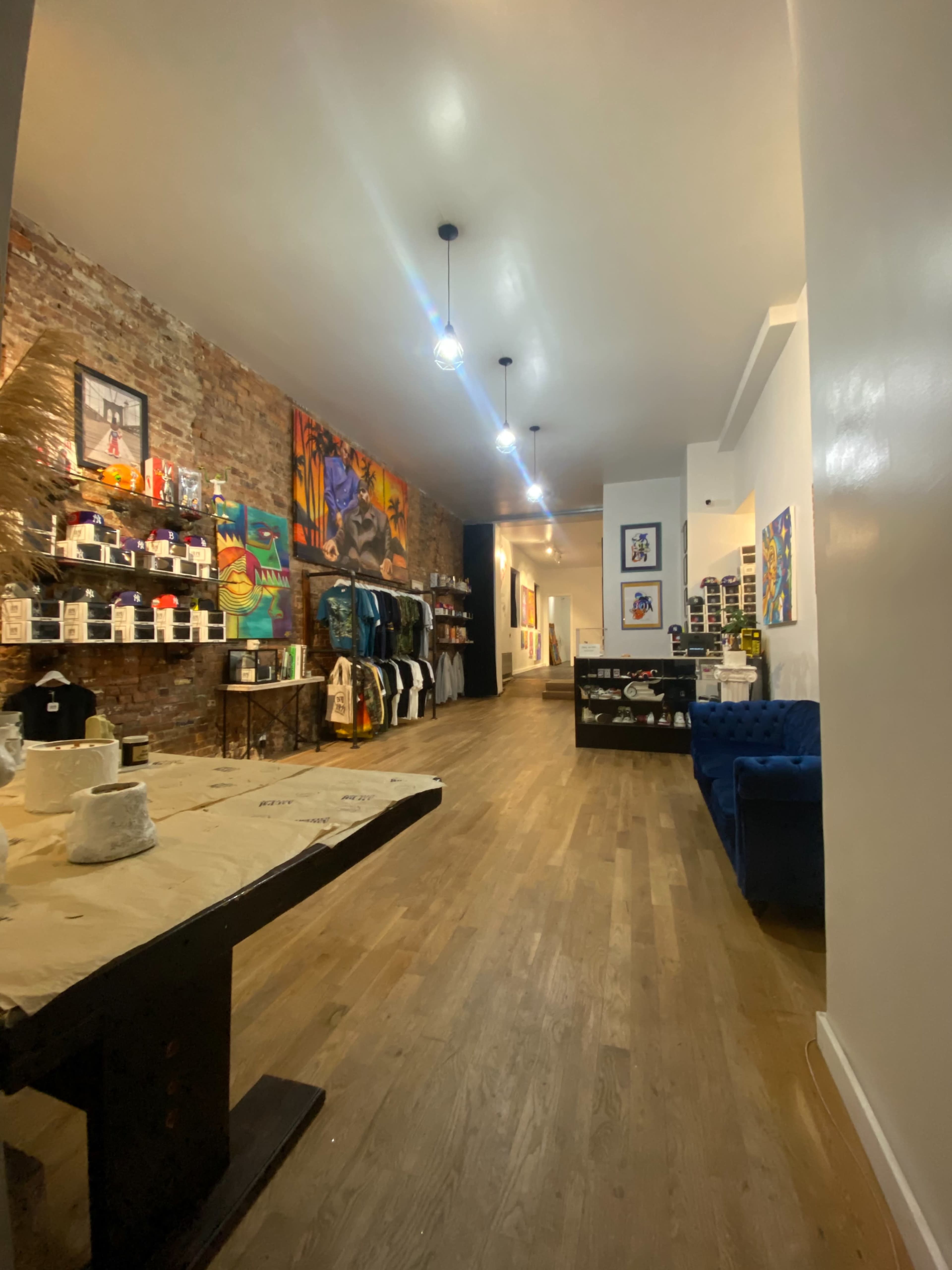 An art gallery featuring exposed brick walls, display shelves with various items, a blue couch, and artwork lining the walls.