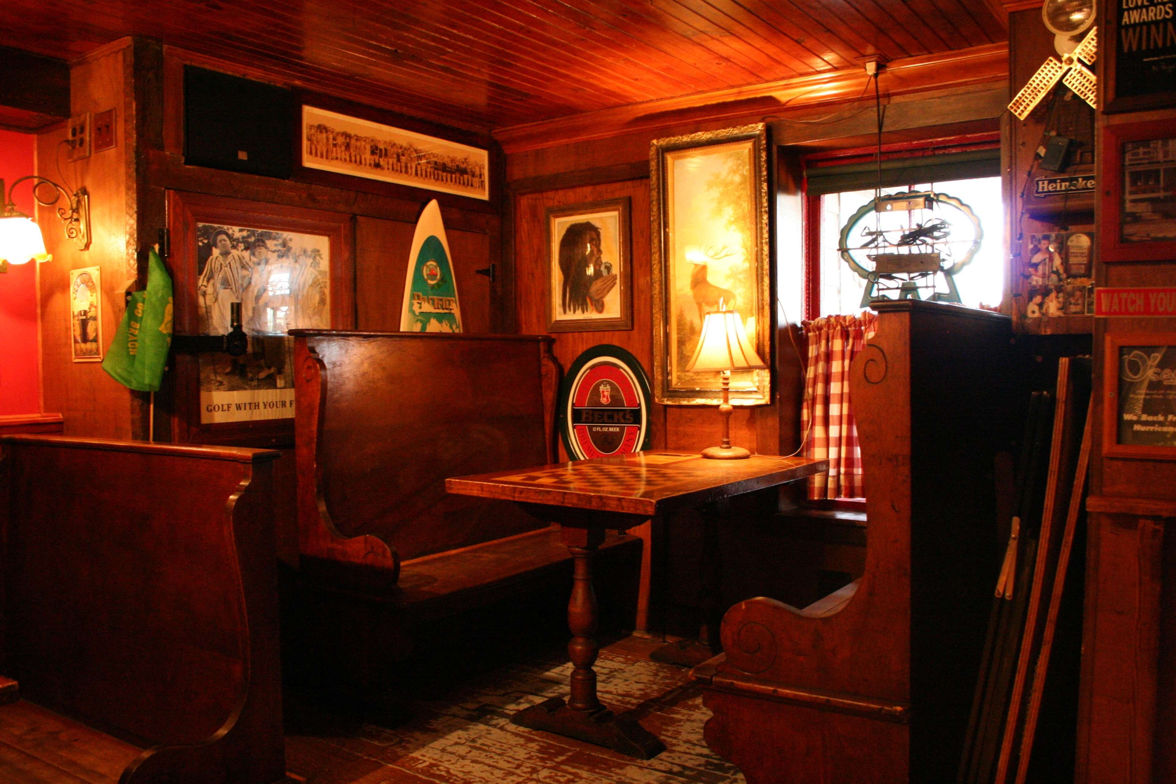 The image shows a rustic wooden dining area with two benches, a table in the center, and framed pictures and decorations on the walls.