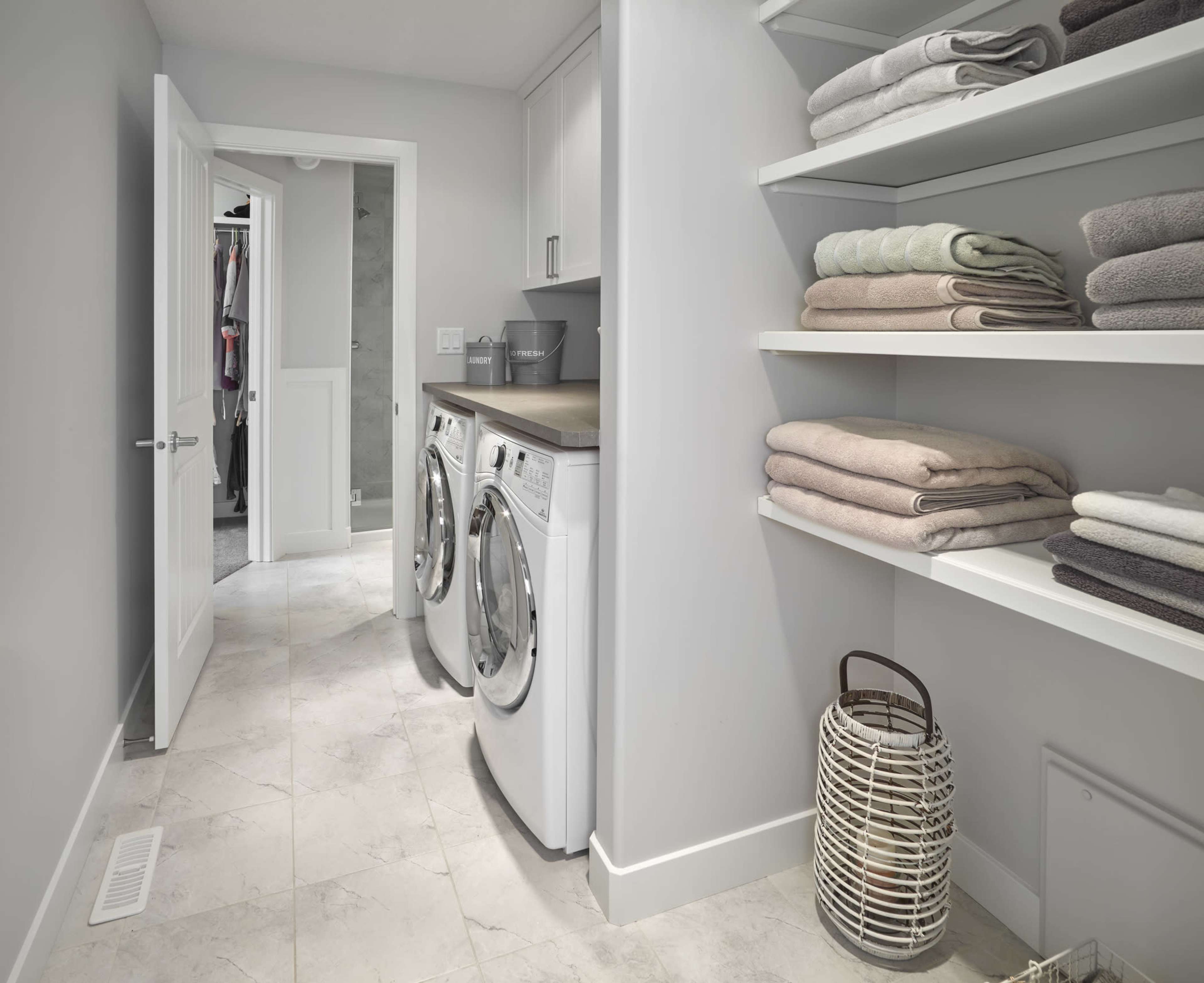 A laundry room features stacked front-loading washers and dryers beside neatly organized shelves of folded towels.