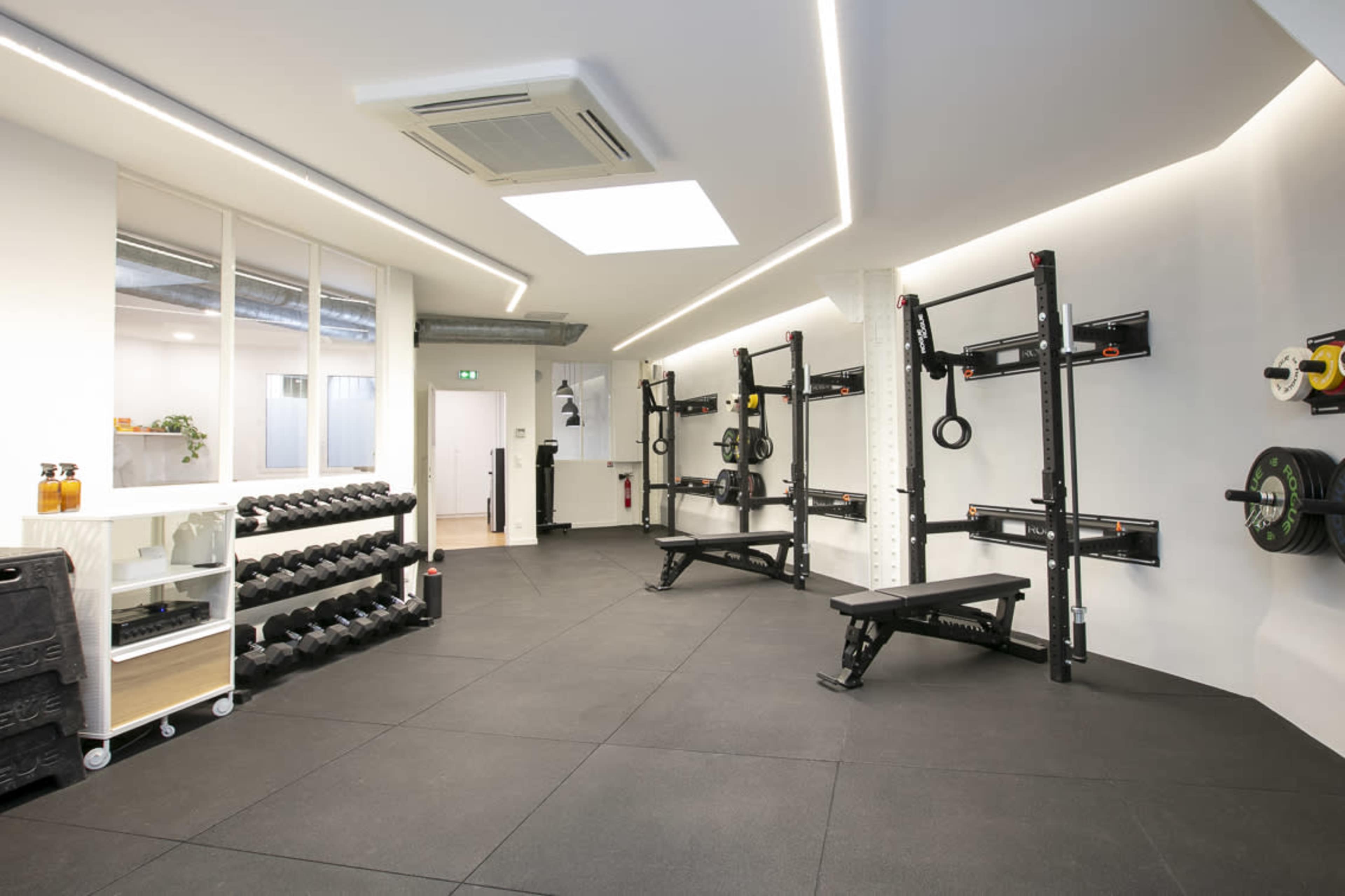 A well-organized gym interior featuring a rack of dumbbells, a weight bench, and wall-mounted strength training equipment in a spacious layout.