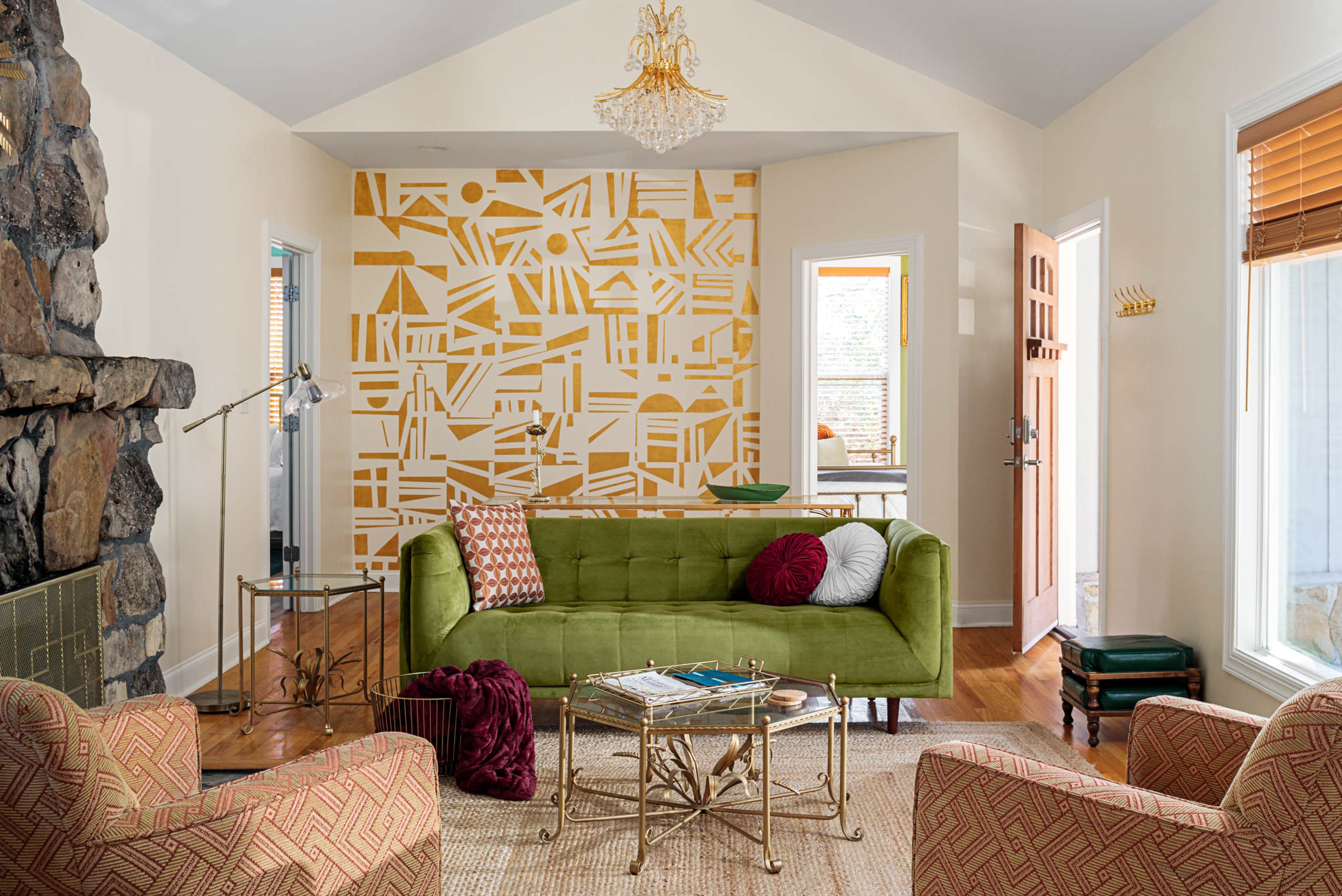 The living room features a green sofa, two patterned chairs, and a geometric accent wall, alongside a coffee table and a stone fireplace.