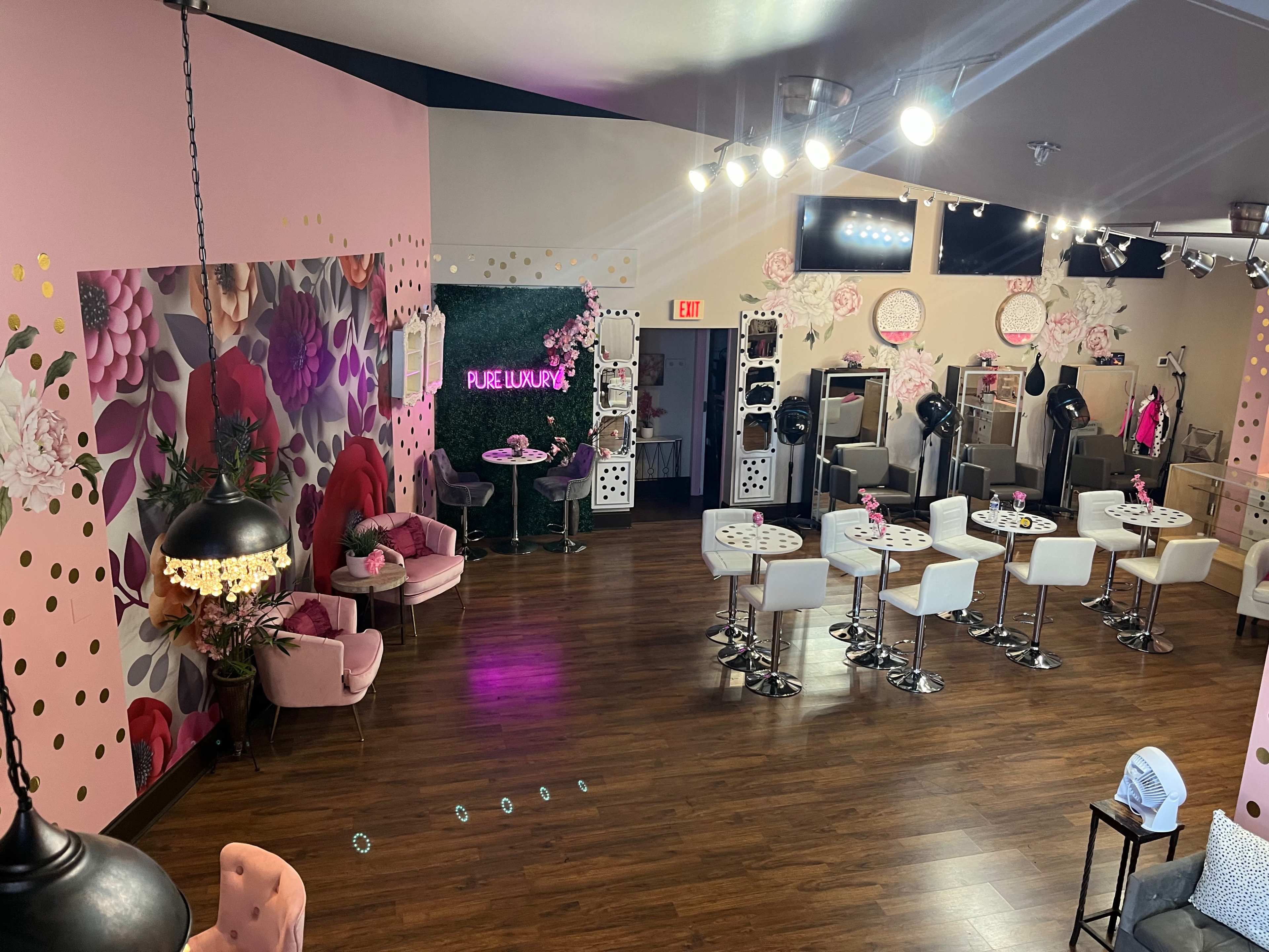 A brightly decorated salon or beauty studio with pink walls, floral accents, and seating areas featuring modern bar stools and tables.