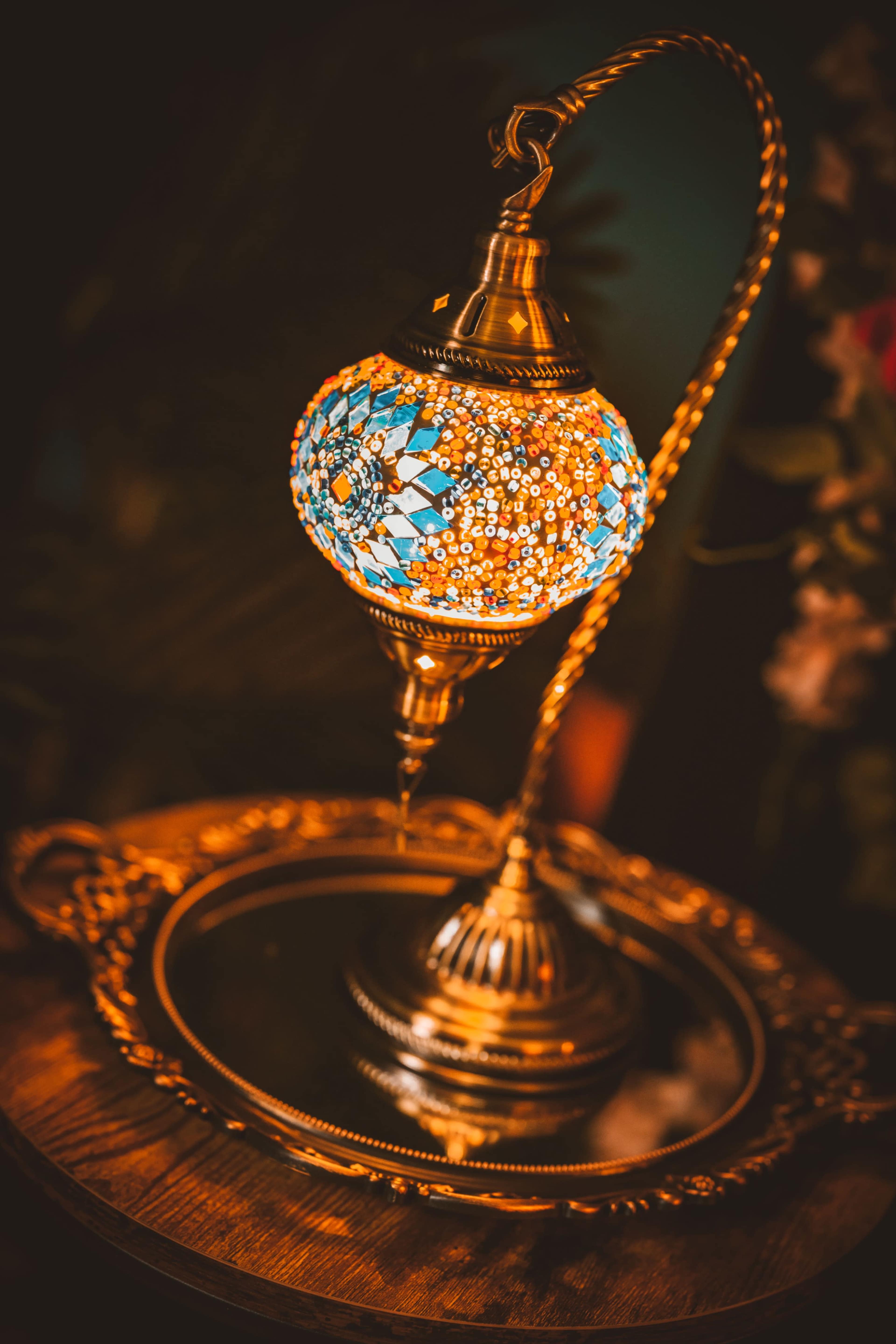 A decorative lamp with a colorful mosaic design sits atop a polished wooden table next to a mirrored tray.