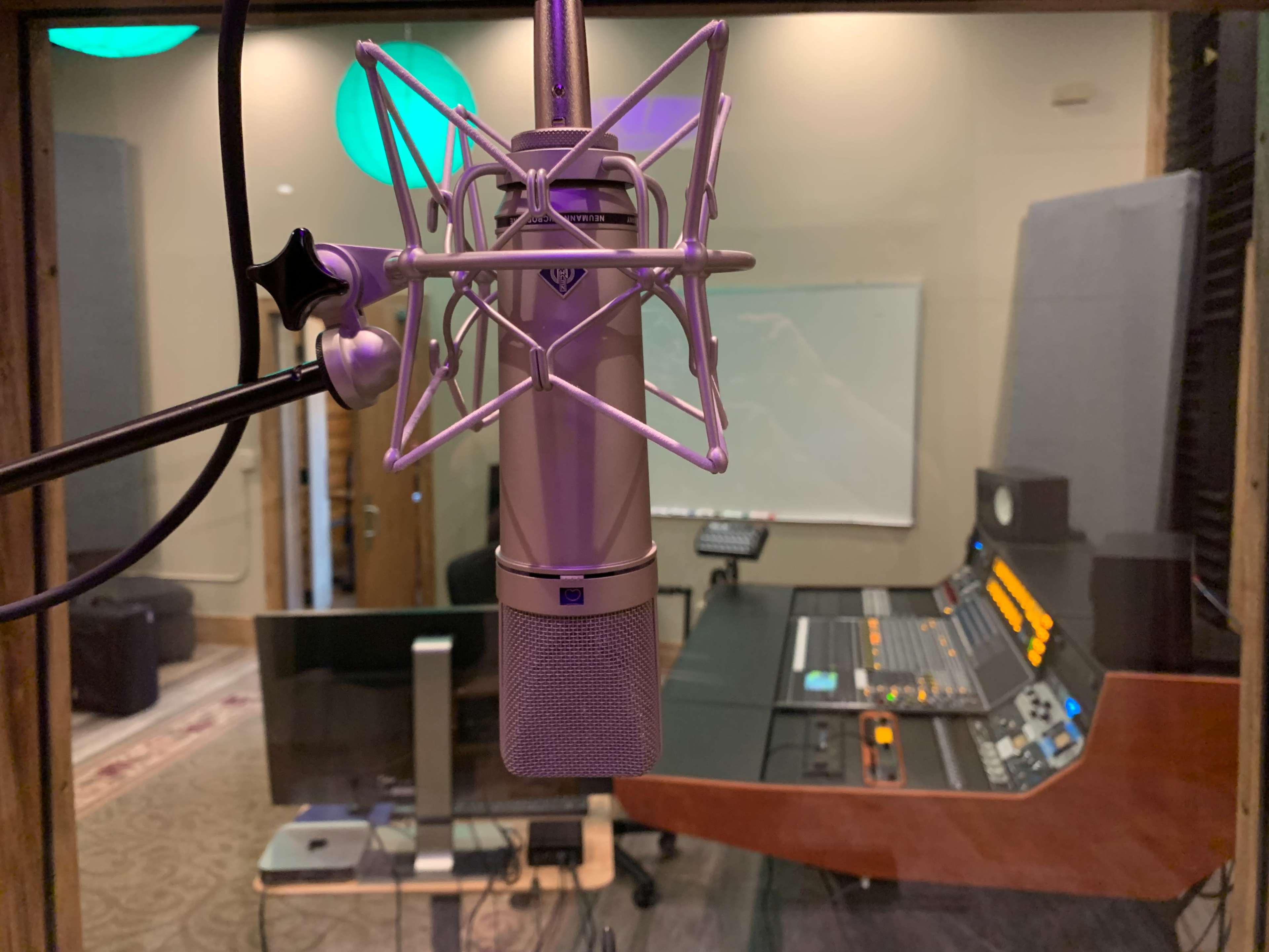 The image shows a microphone with a pop filter in a recording studio, with a mixing console and a blank whiteboard visible in the background.