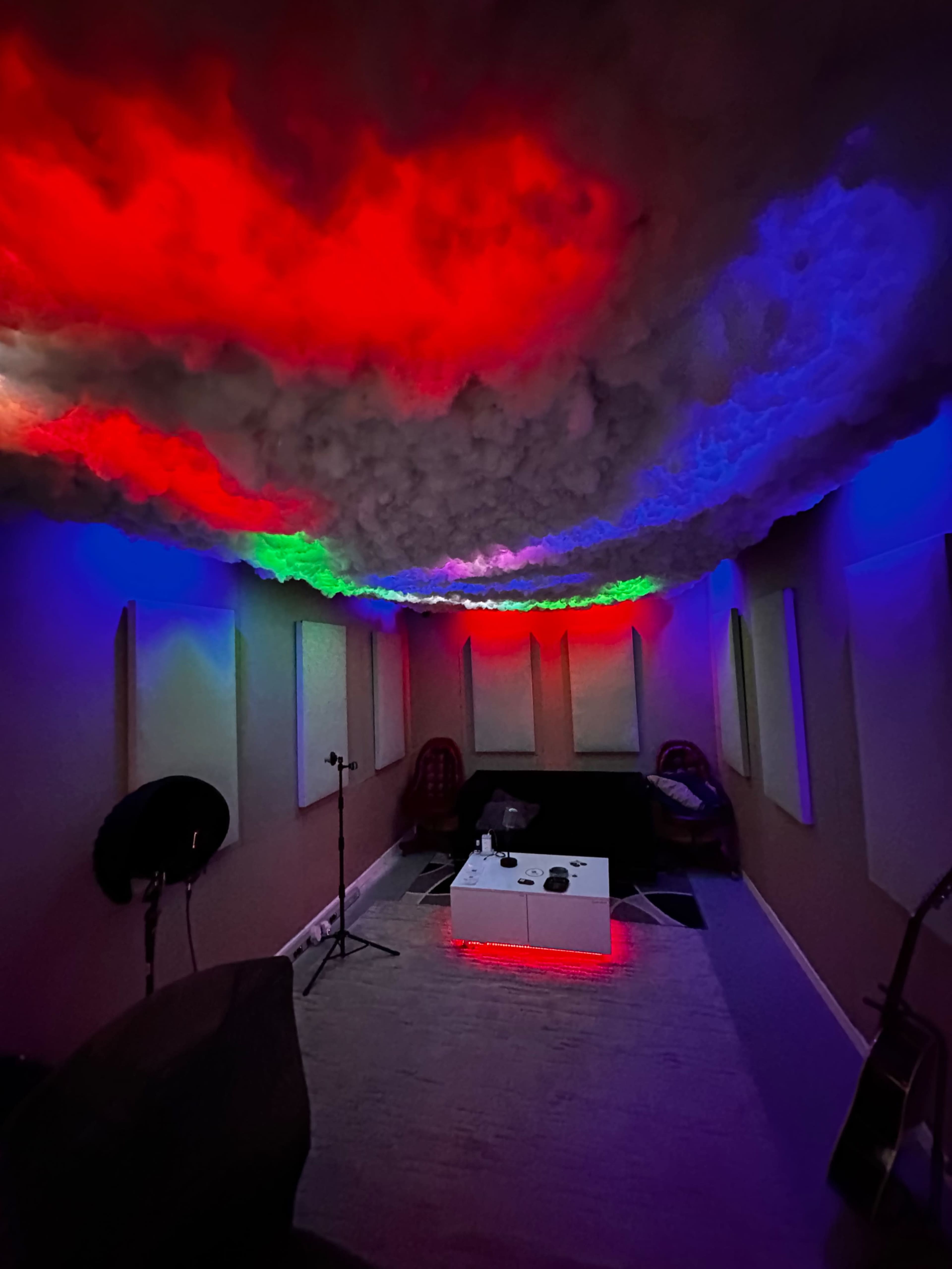 A cozy room with a cloud-like ceiling adorned with colored lights, a central coffee table, and musical instruments in the corners.